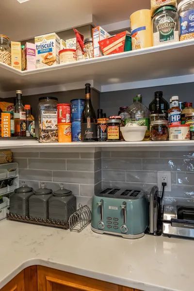 A kitchen with shelves filled with lots of food and a toaster.