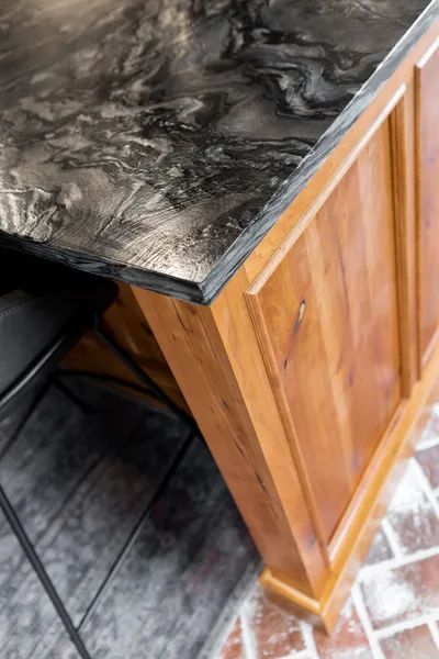 A kitchen island with a black granite counter top and wooden cabinets.