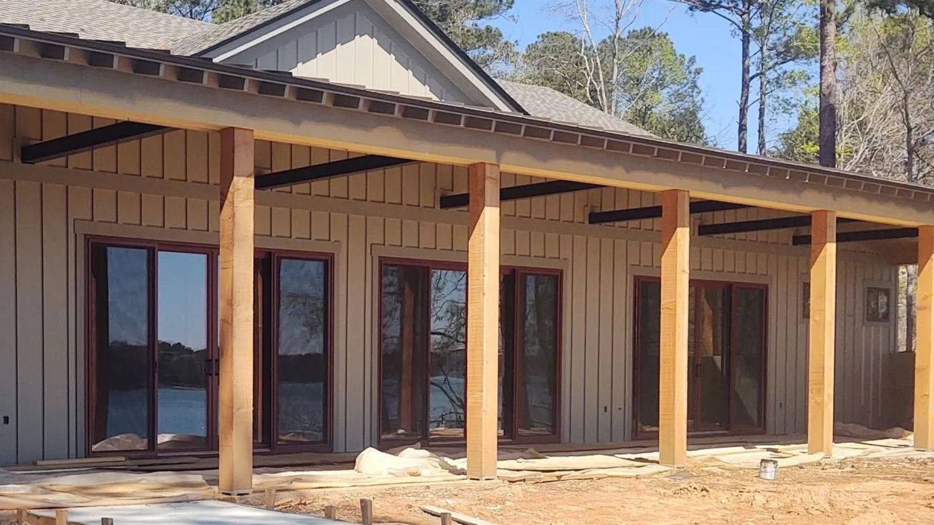 Tan-sided house with wooden columns and dark-framed doors, overlooking a lake.