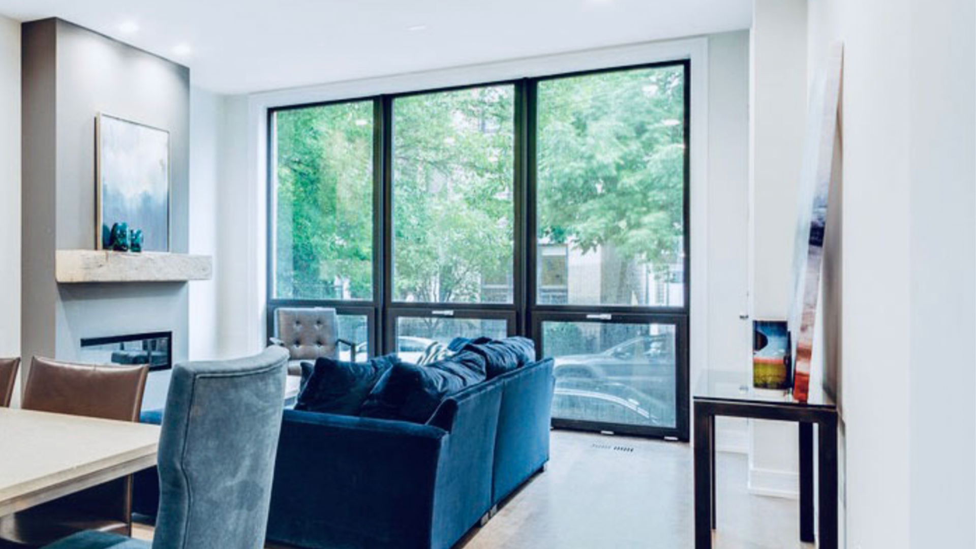 A living room with a blue couch , chairs , a table and a fireplace.