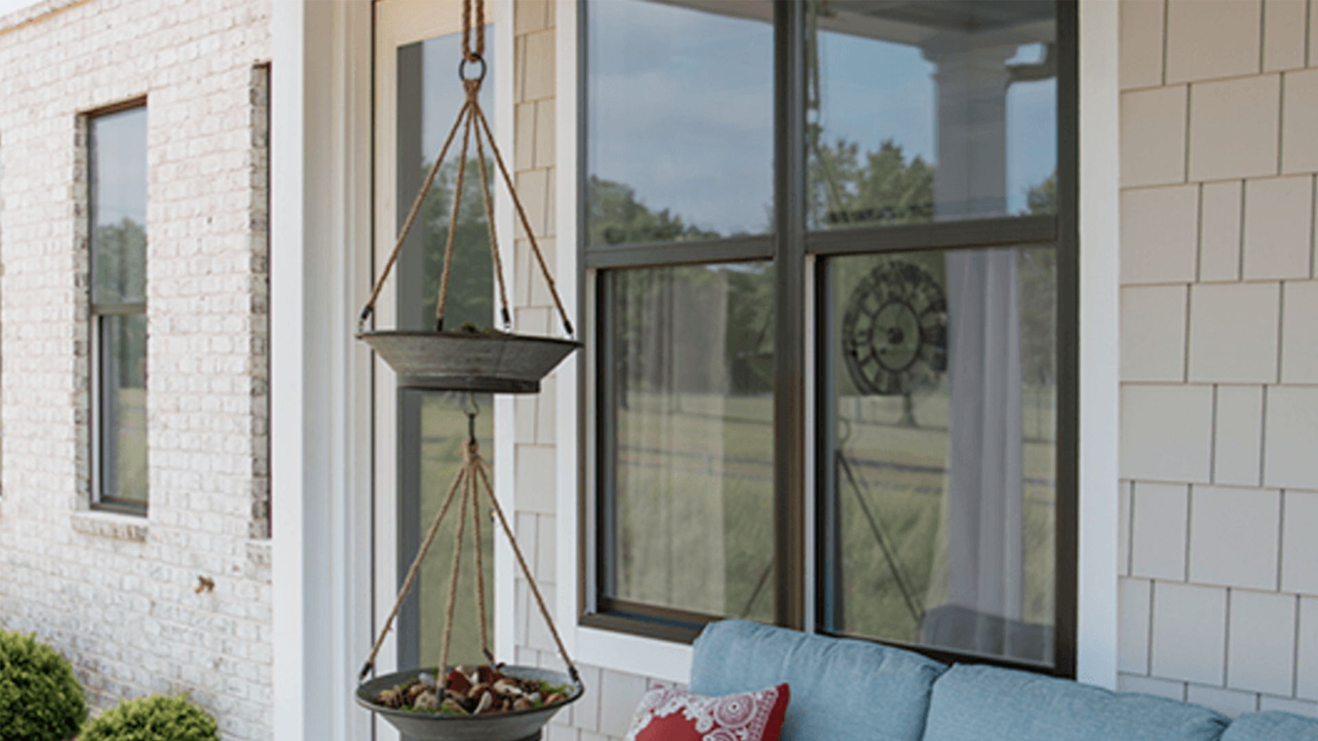 A porch with a blue couch and a bird feeder hanging from the window.