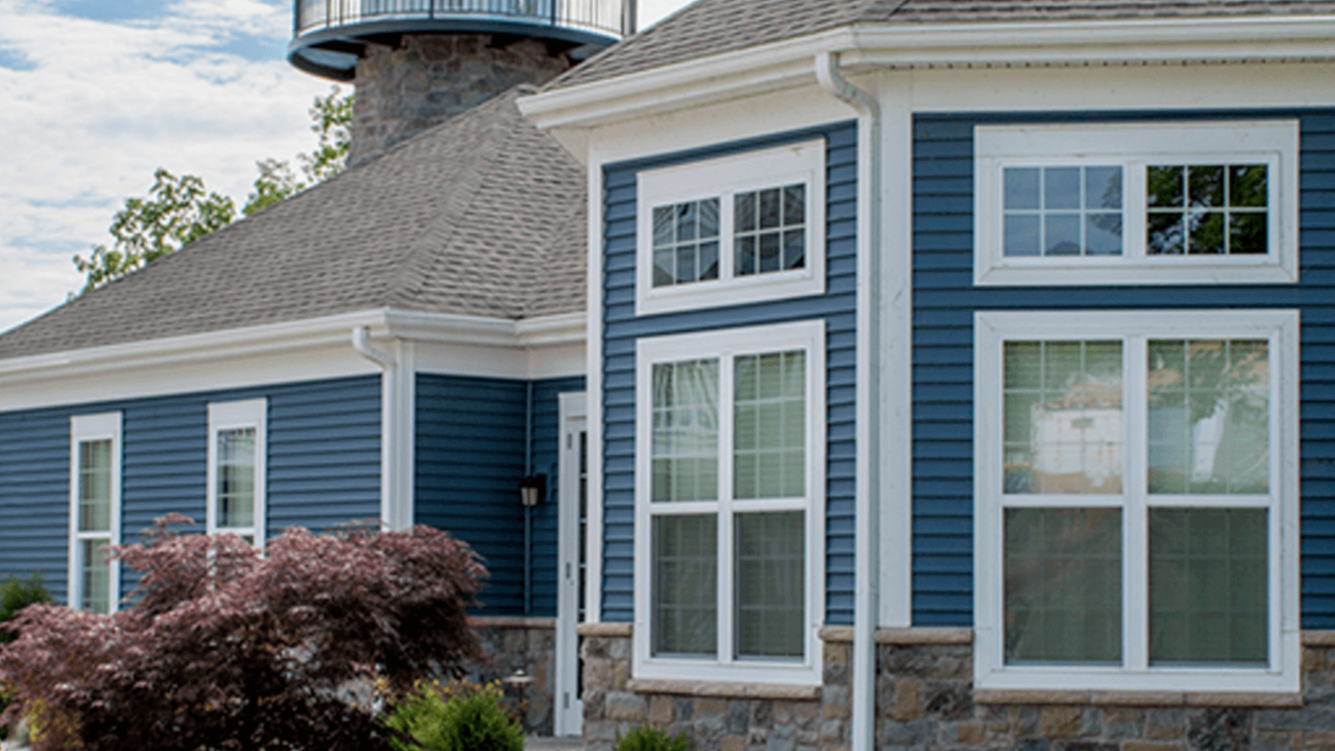 A blue and white house with a lighthouse in the background.