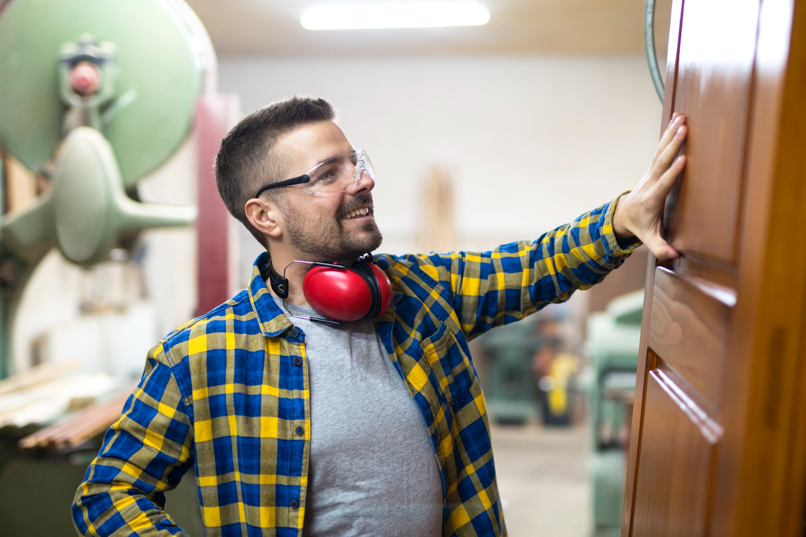 Man in yellow plaid shirt and red headphones reaches to touch a wooden door indoors