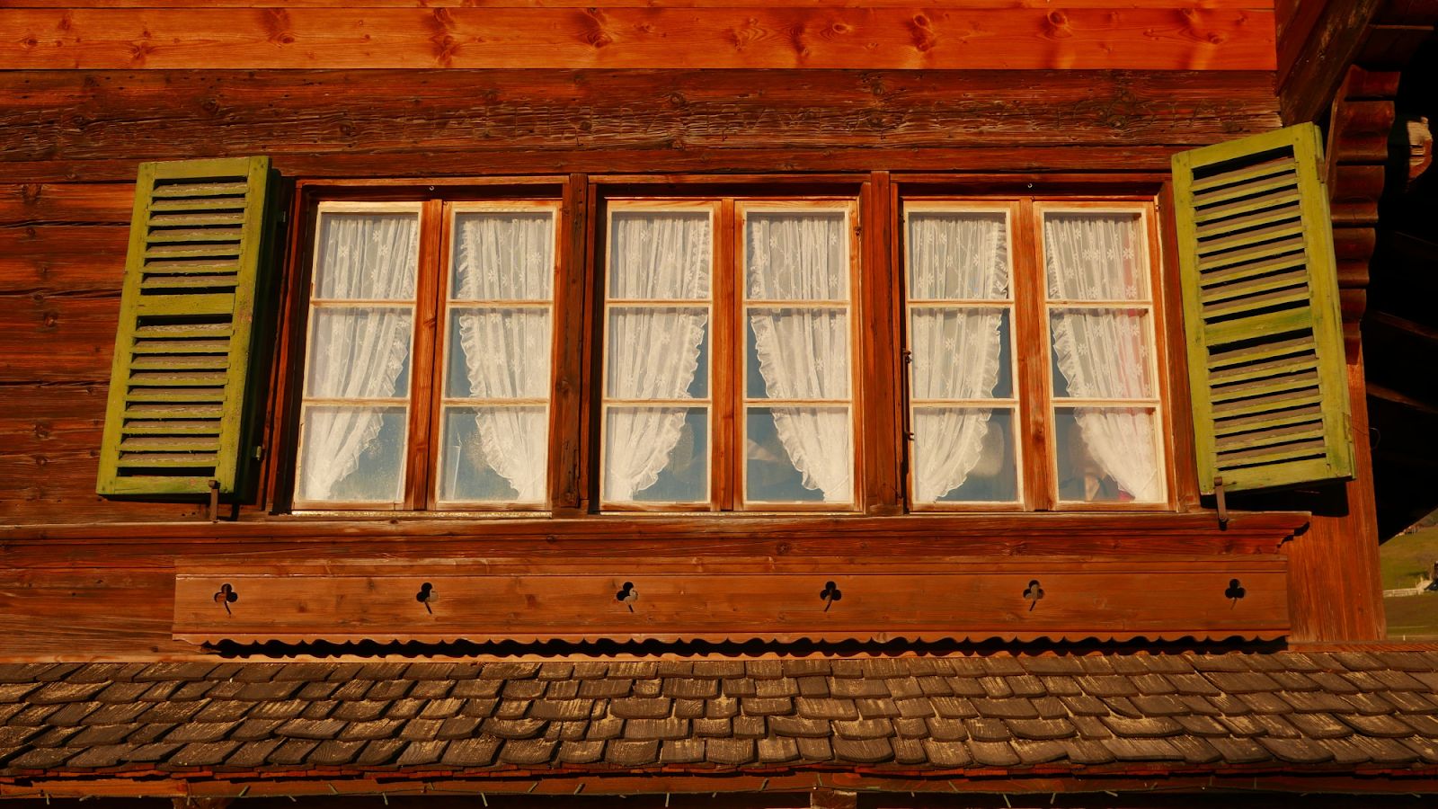 Close-up of traditional wooden house window with lace curtains and green shutters on a rustic exter