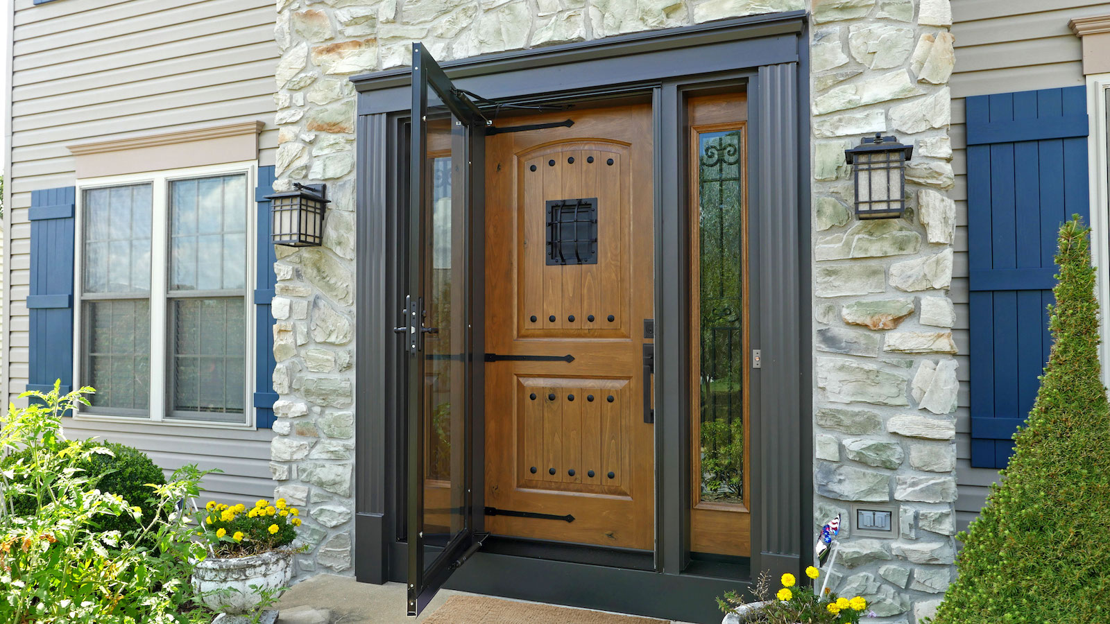 Elegant wooden front entry door with decorative glass storm door set in a stone exterior home facad