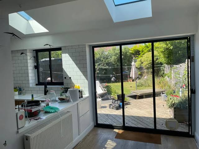 “Modern kitchen with large black-framed sliding glass patio doors opening onto a backyard deck.”