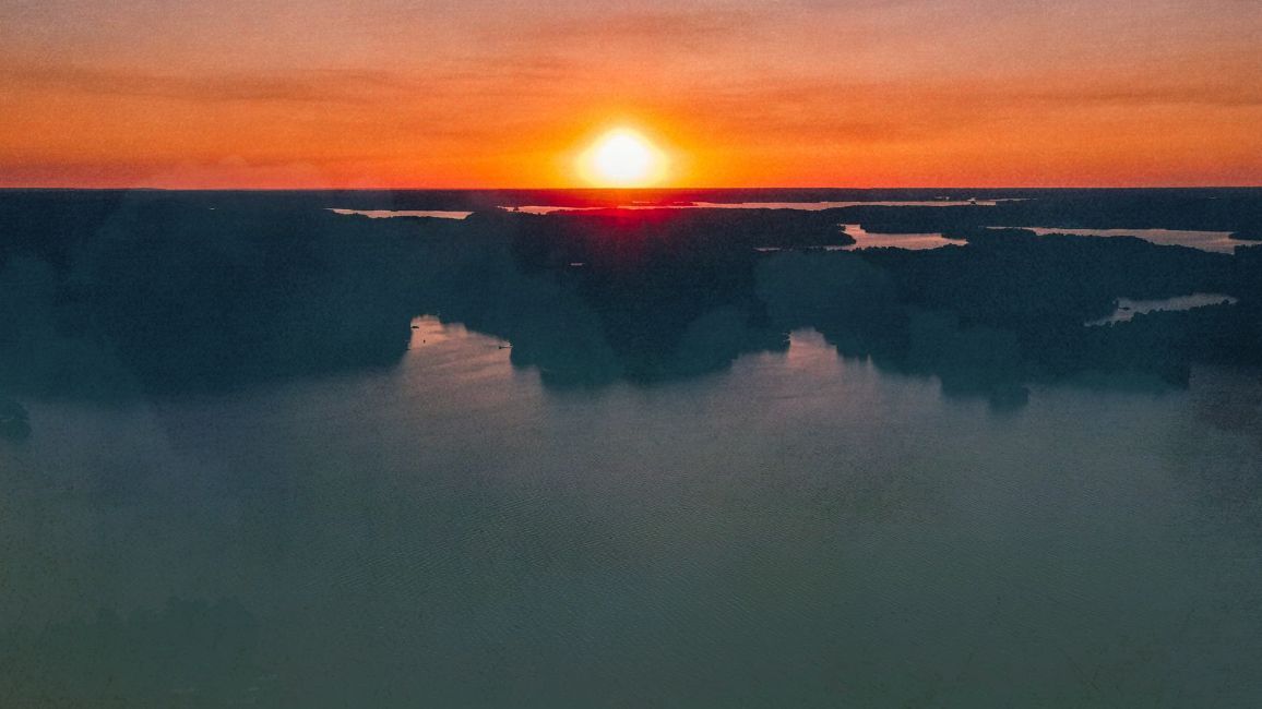 the sun is setting over lake martin, al with clouds in the foreground .