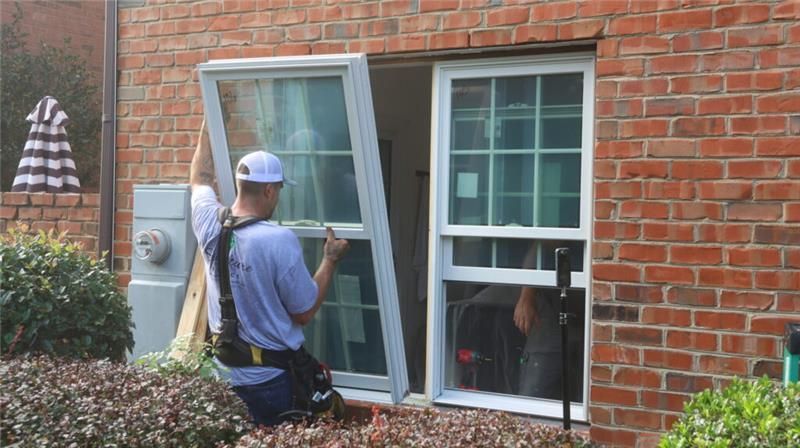 Technicians installing replacement windows in a brick home exterior during a residential window upgrade.