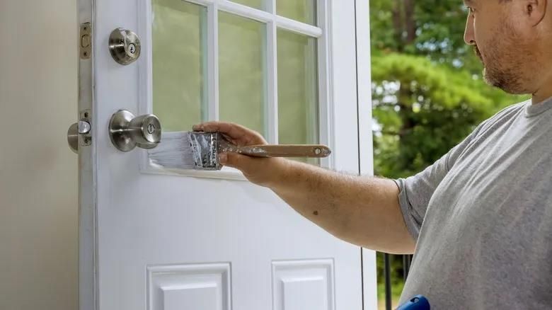 Professional applying fresh paint around a residential entry door lock and frame during home
