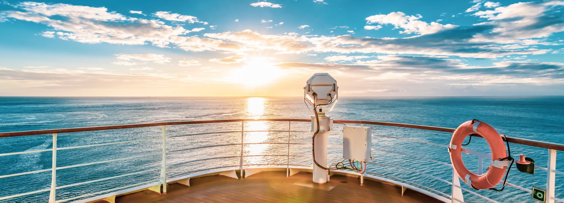 View from a ship's deck at sunset over the ocean. A life preserver hangs on the railing.