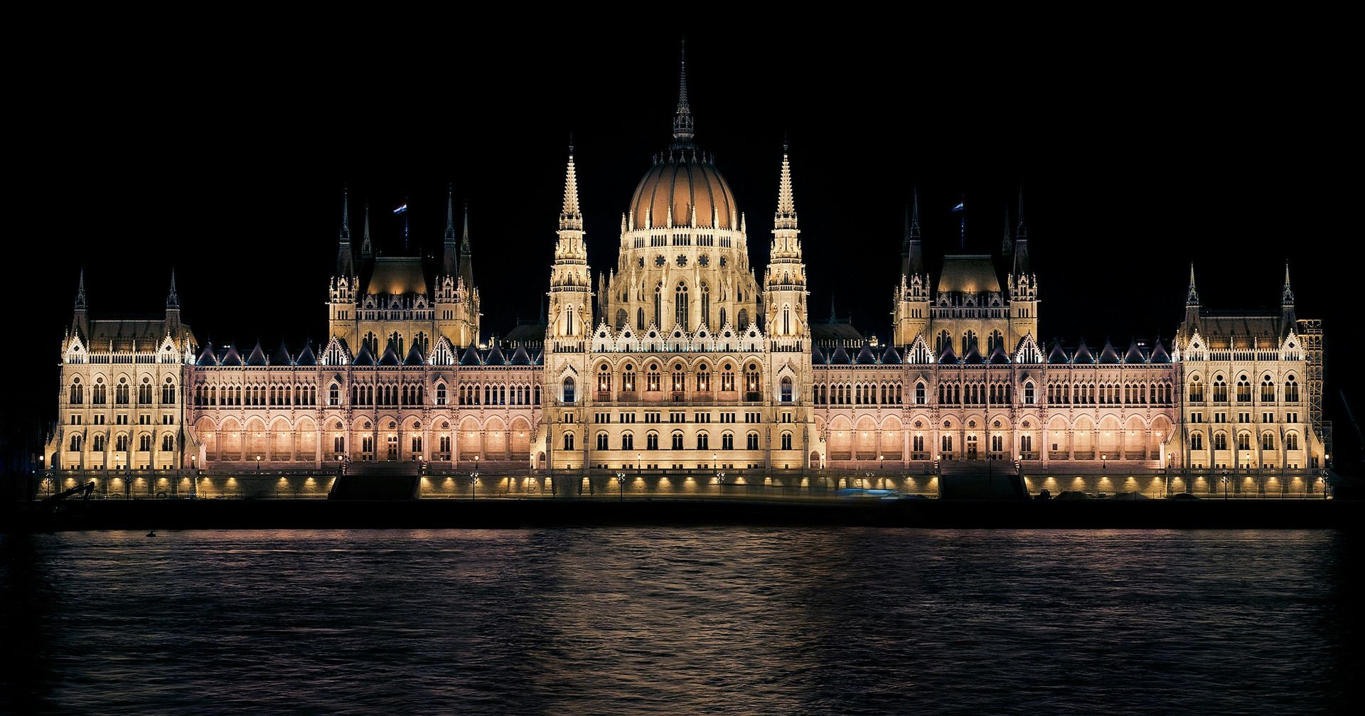 Hungarian Parliament Building illuminated at night, reflecting in the water.