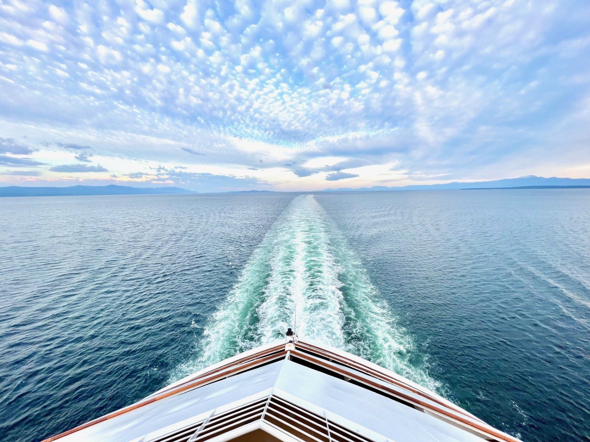 Boat sailing on a calm ocean with a wake trailing behind, under a blue sky with clouds.