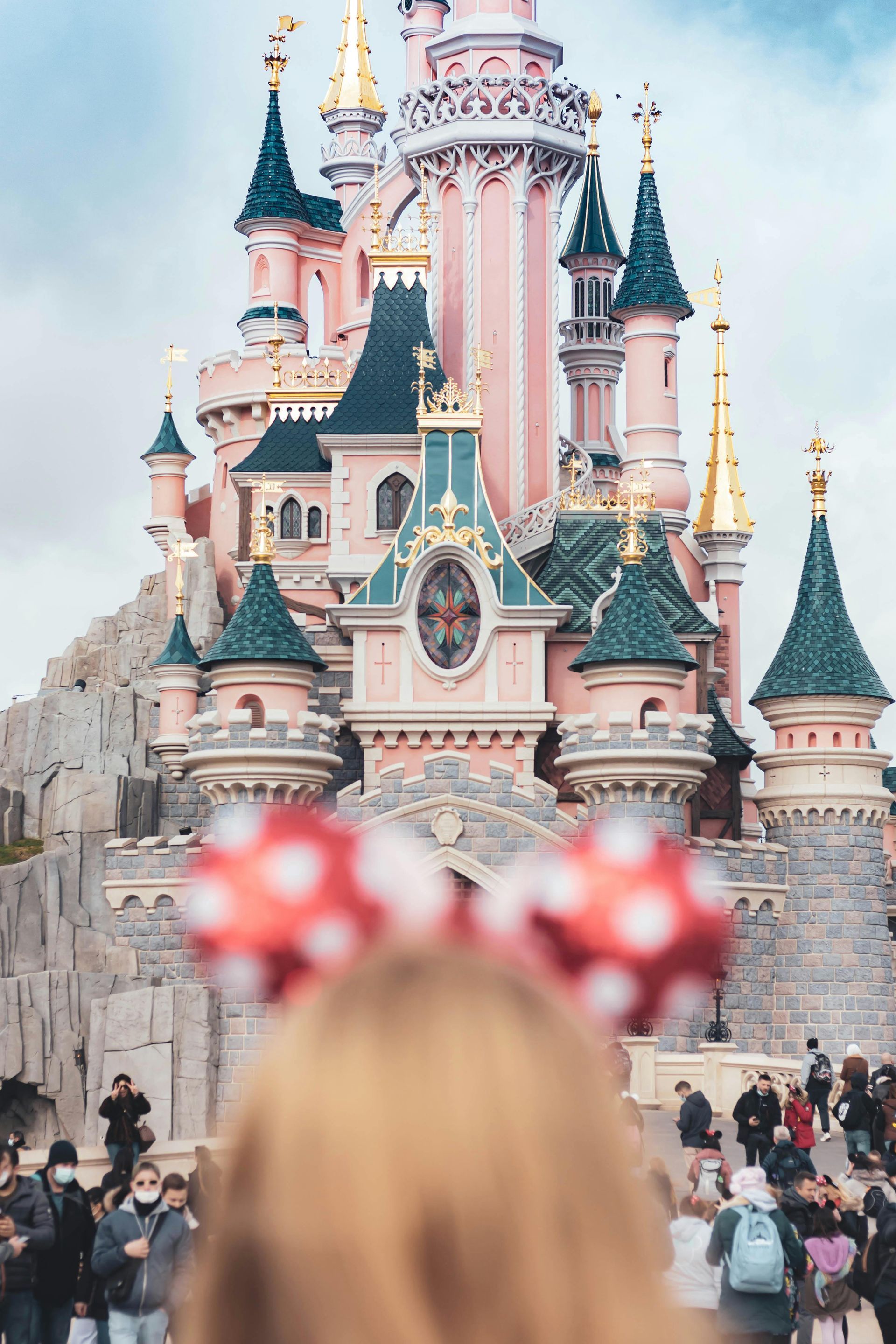 Person wearing Minnie Mouse ears in front of Sleeping Beauty Castle at Disneyland Paris.