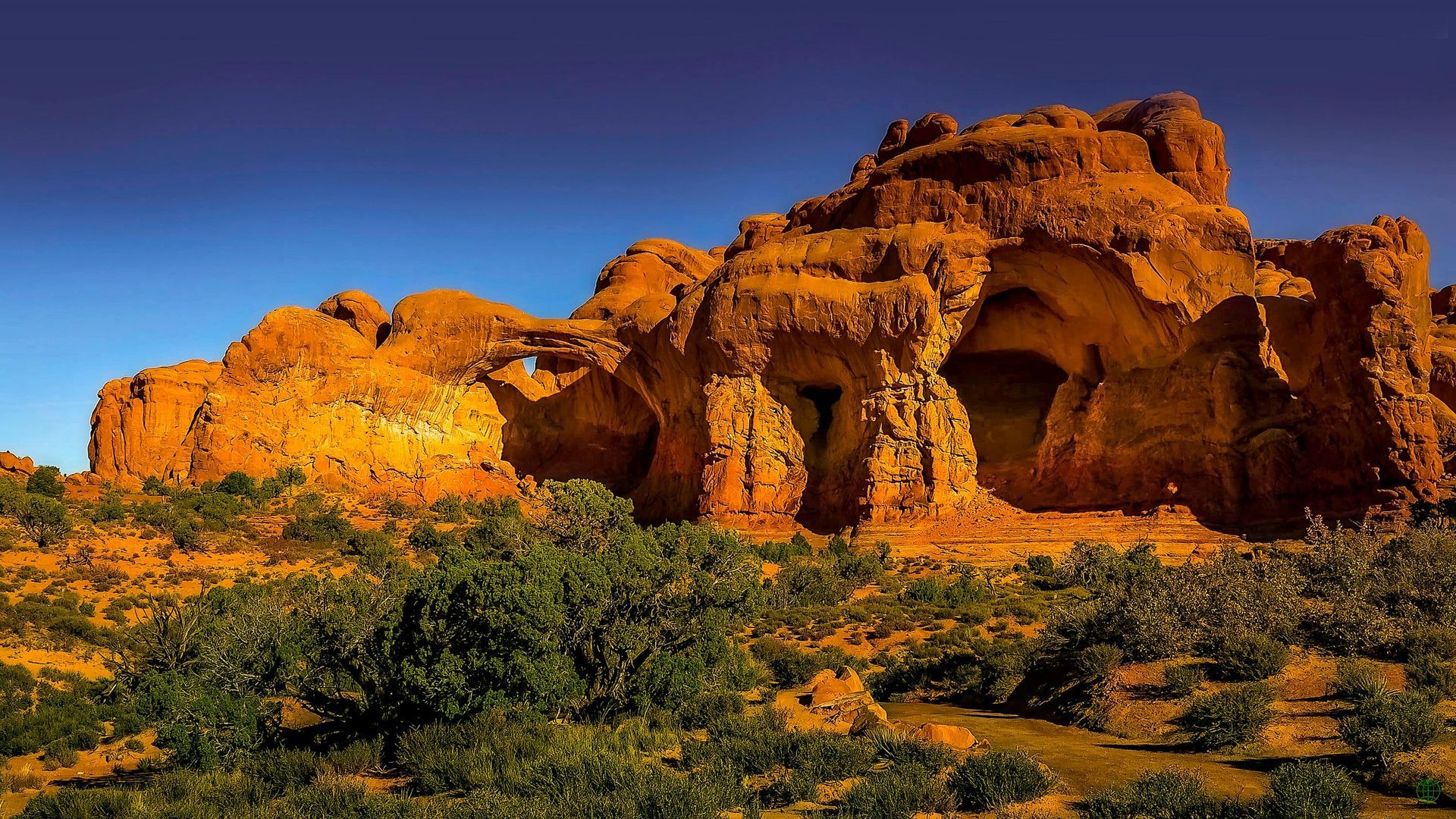 Eroded sandstone rock formations with arched openings and a blue sky in a desert landscape.