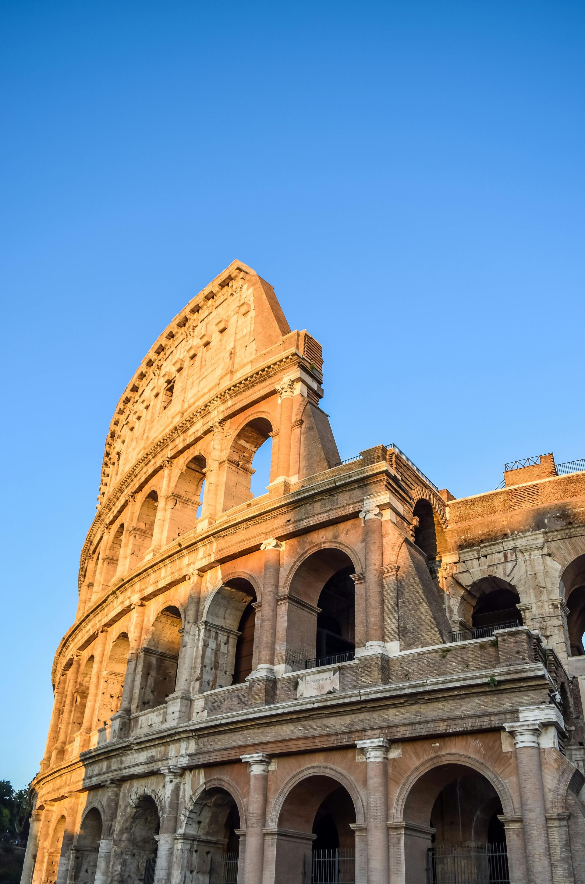 Colosseum, Rome, Italy. Ancient Roman amphitheater exterior against a blue sky. Sunlight highlights brick and stone.