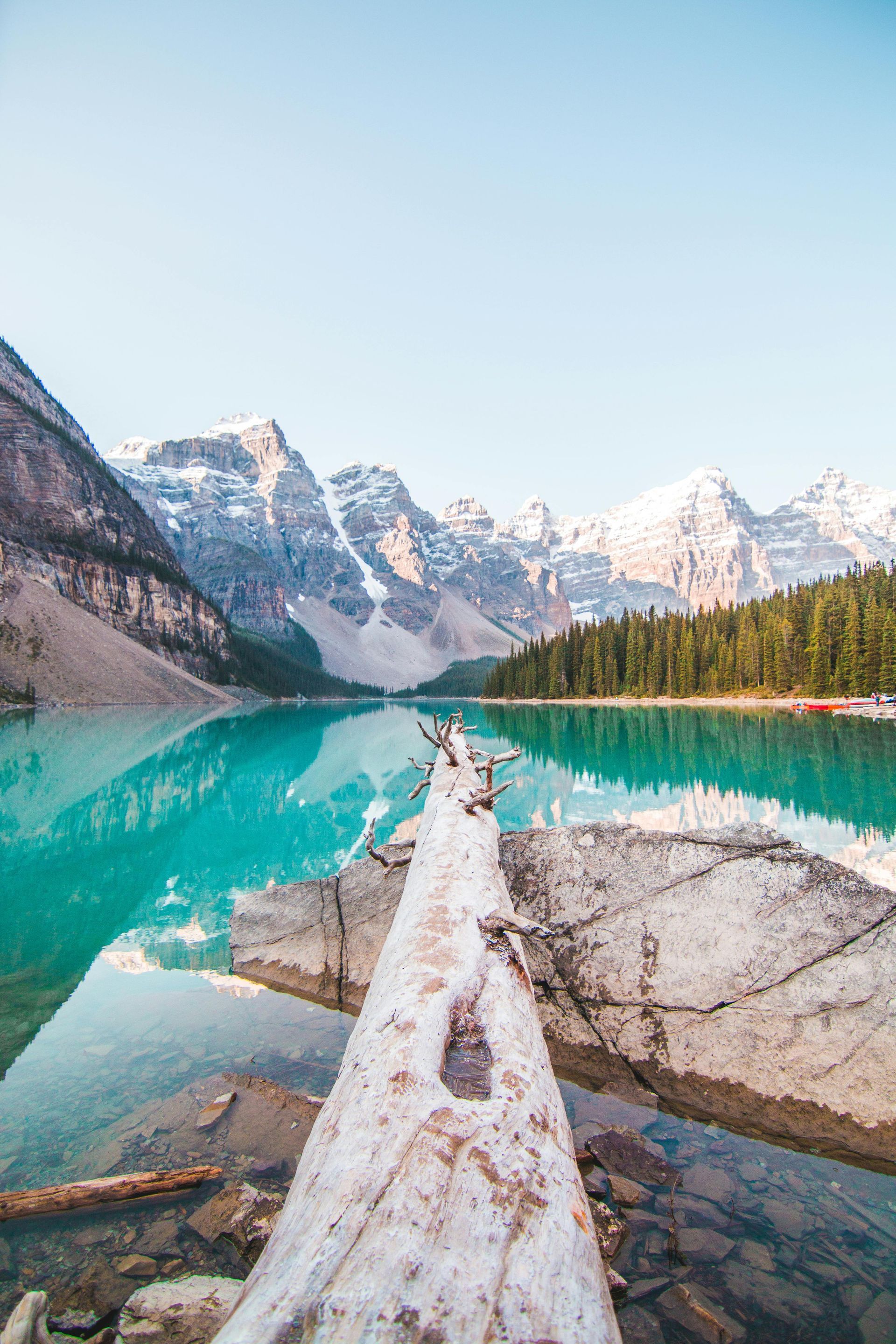 Turquoise lake with snow-capped mountains and a log in the foreground.