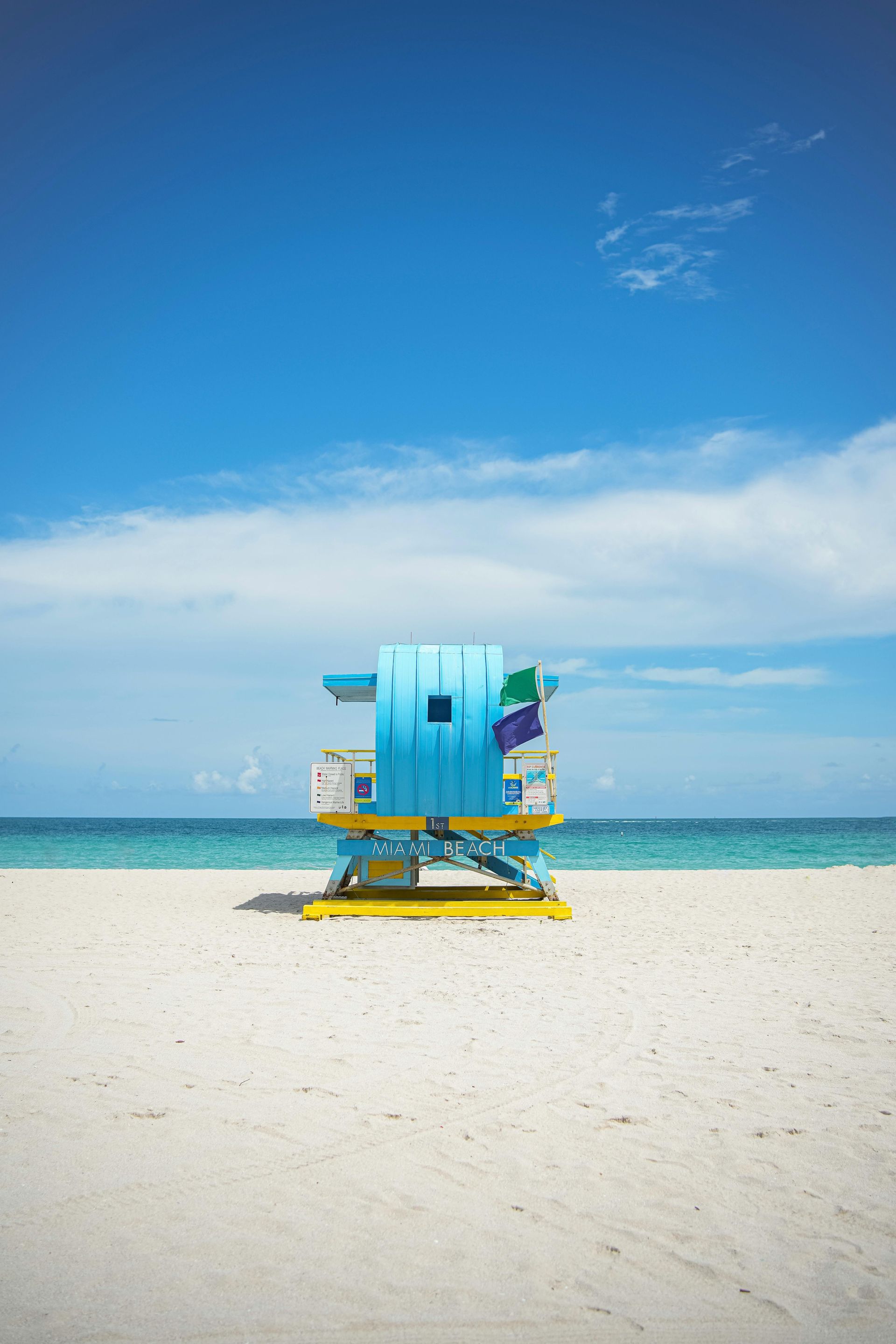 Blue lifeguard station on white sandy beach under a bright blue sky.
