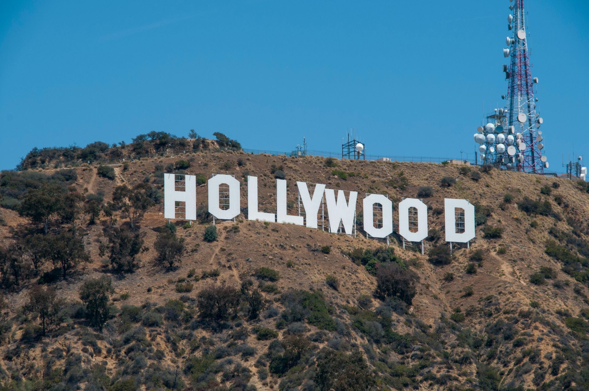 The Hollywood sign on a brown hillside with a blue sky, radio tower in background.