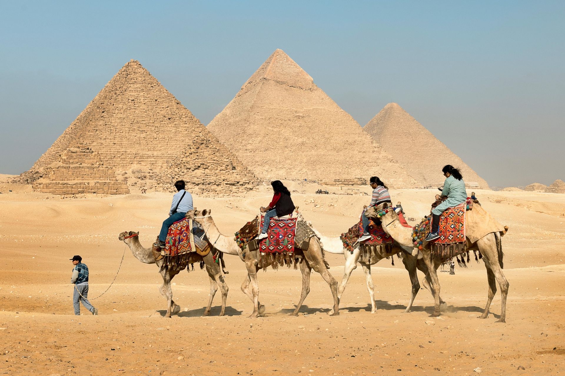 People ride camels near the Giza pyramids in Egypt. Desert landscape, blue sky.