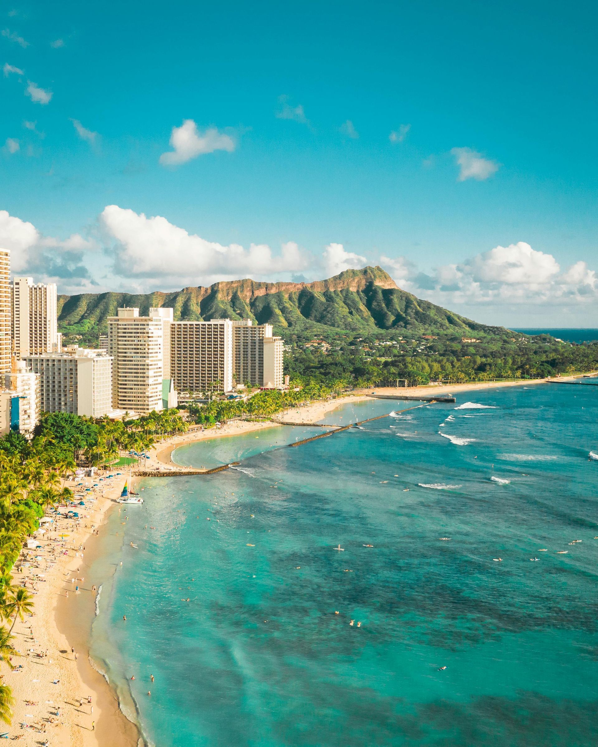 Waikiki Beach with turquoise water, white sand, hotels, lush green foliage, and Diamond Head crater under a blue sky.