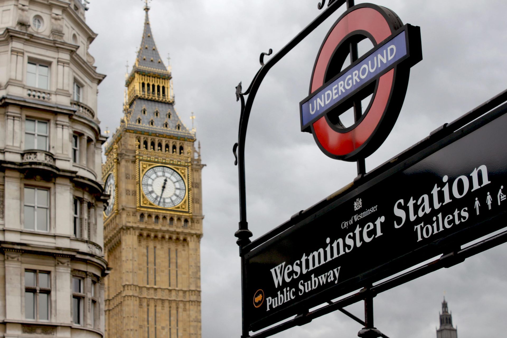 Big Ben clock tower next to Westminster Station sign, London Underground logo, overcast sky.