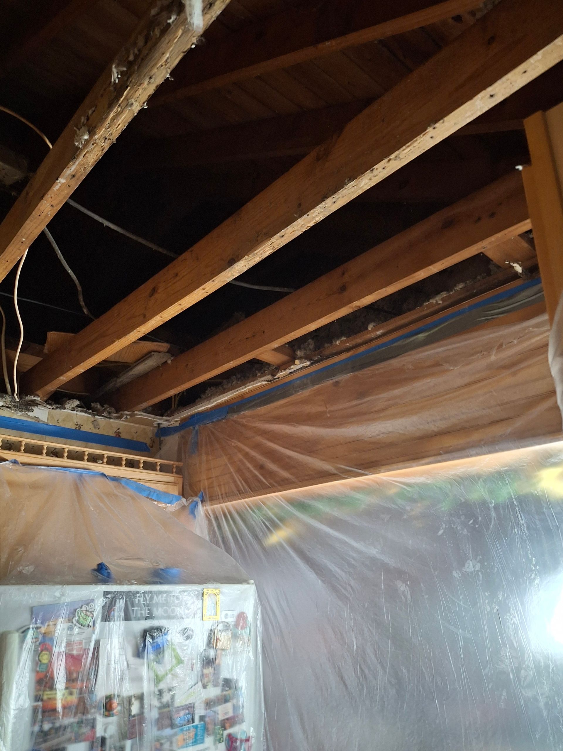 A refrigerator is sitting under a wooden ceiling covered in plastic.