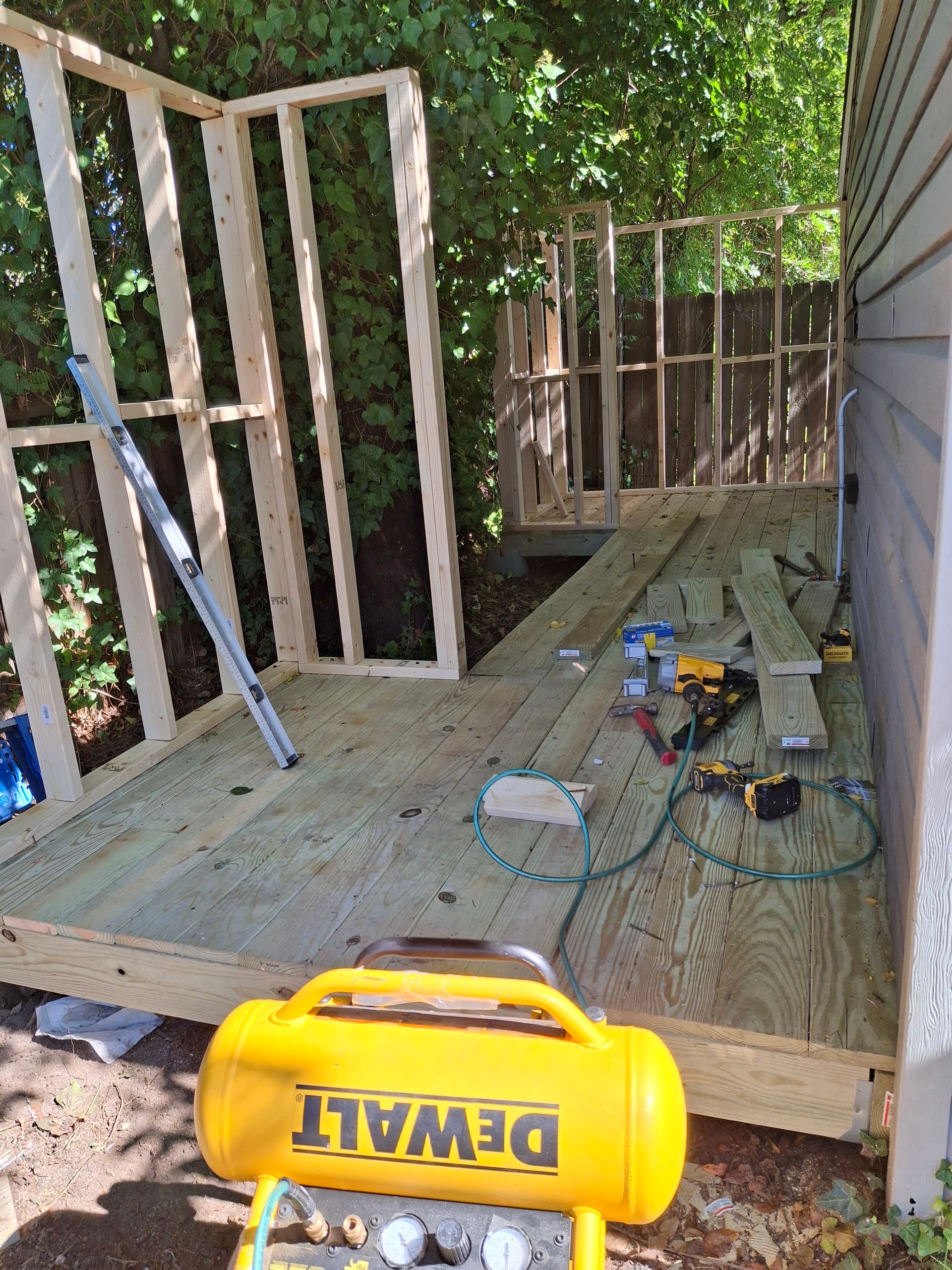 A yellow dewalt air compressor is sitting next to a wooden deck.