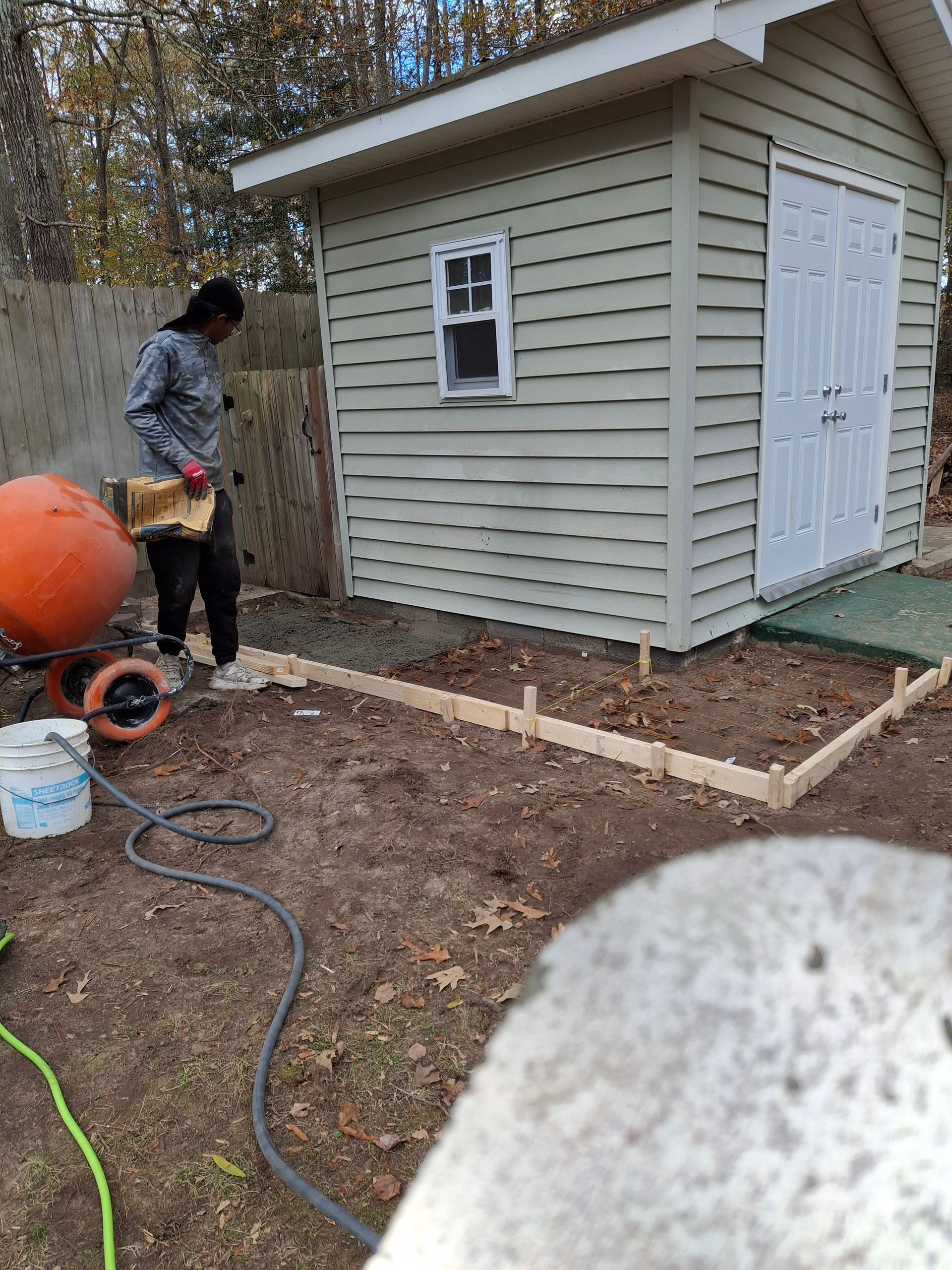 A man is standing in front of a shed in a backyard.