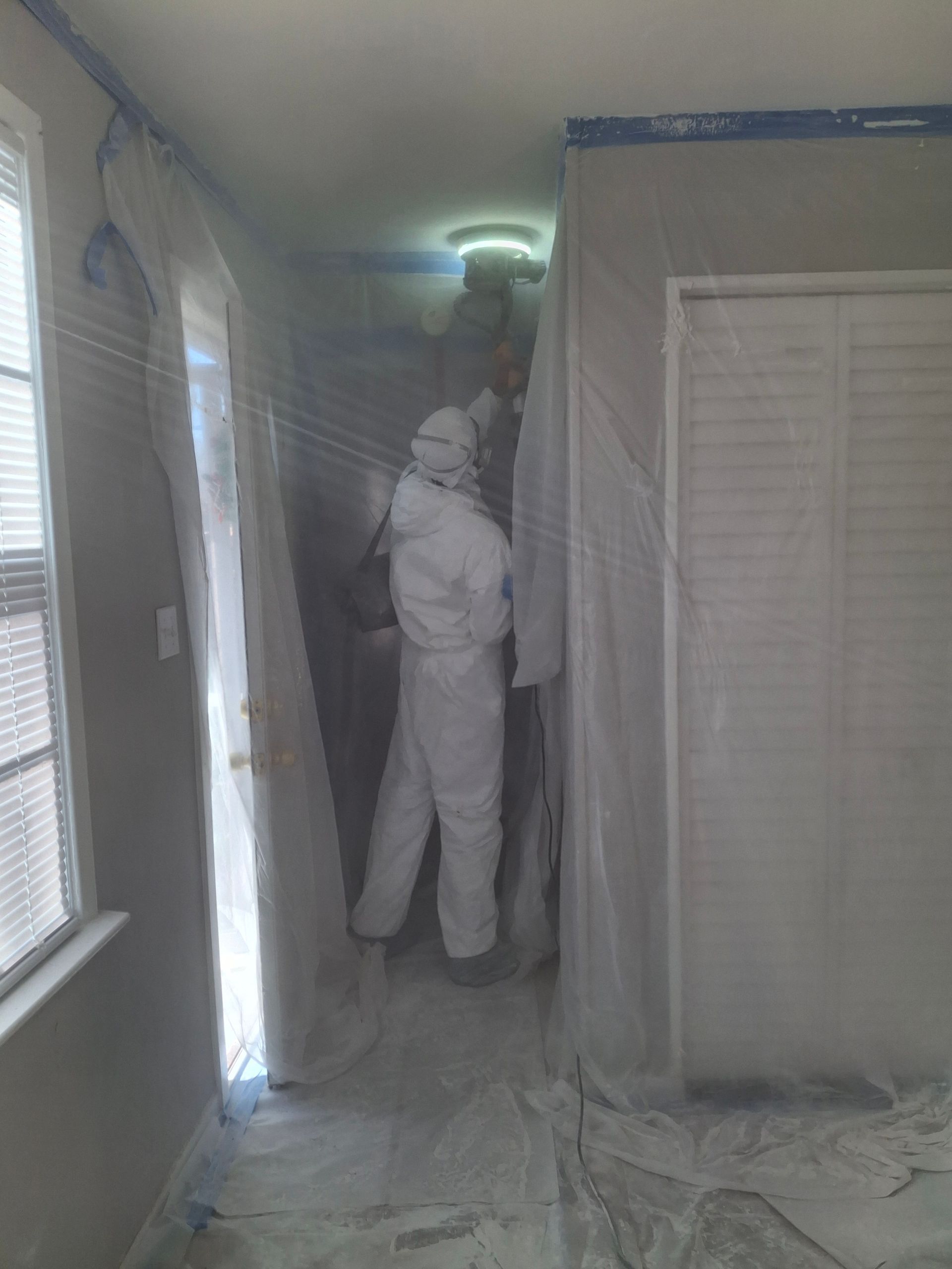 A man in a protective suit is spray painting a wall in a room.