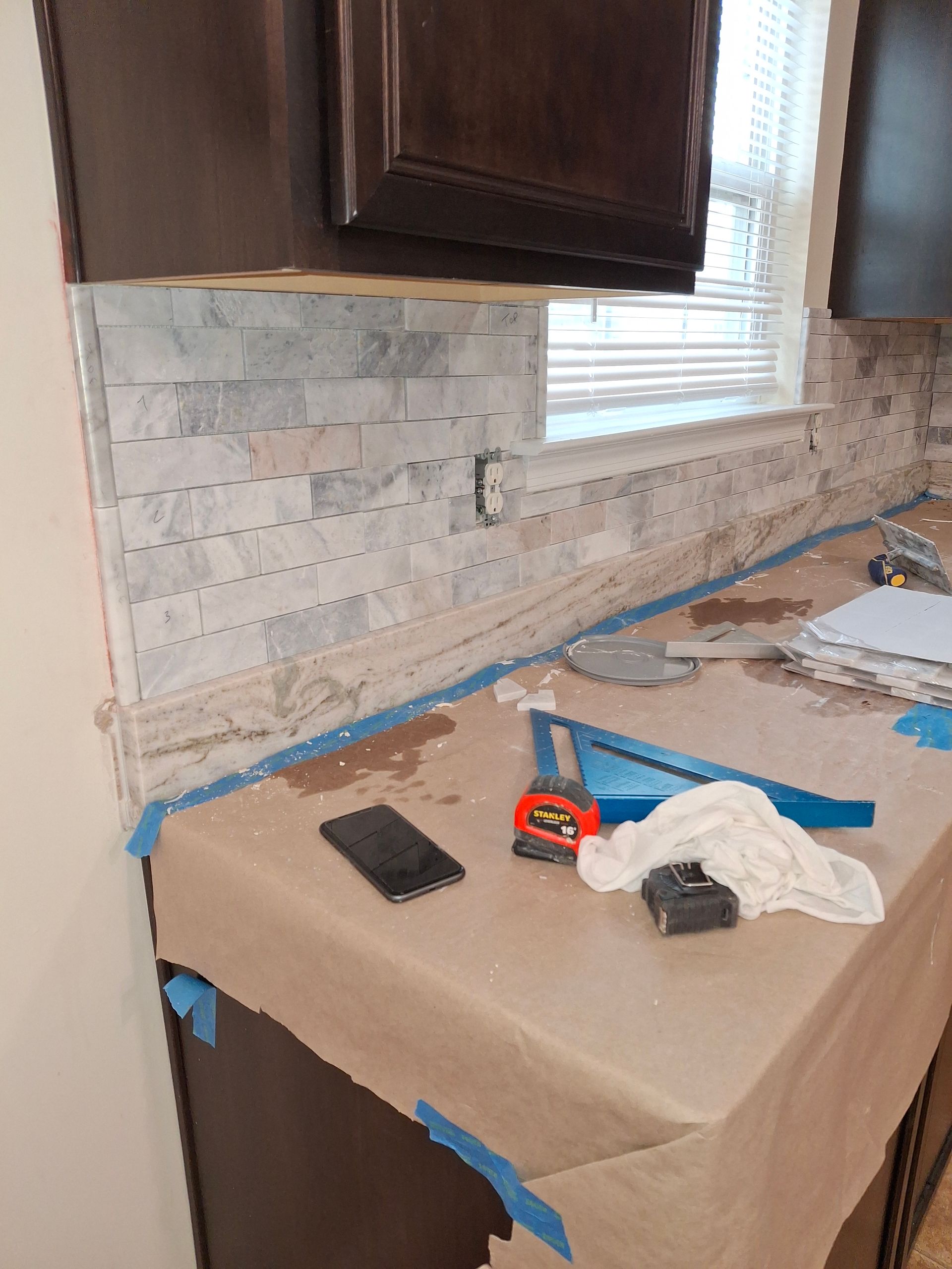 Kitchen counter covered with protective paper and blue tape during backsplash renovation.