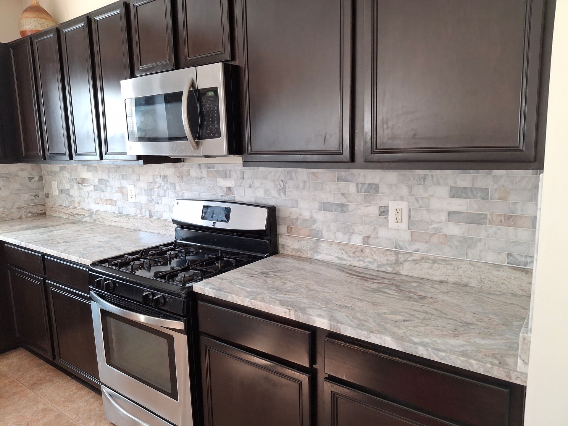 Modern kitchen with dark wood cabinets, stainless steel stove and microwave, and light stone countertops