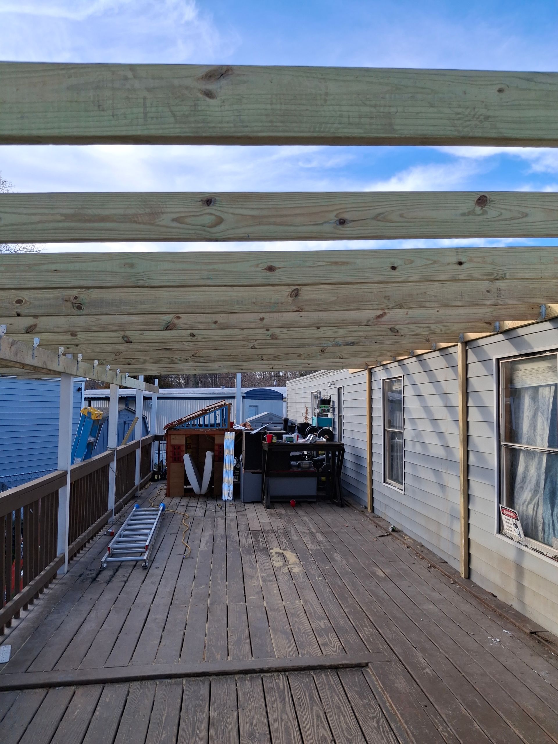 Wooden rooftop deck with pergola beams, ocean view, and a small table and chairs at the far end