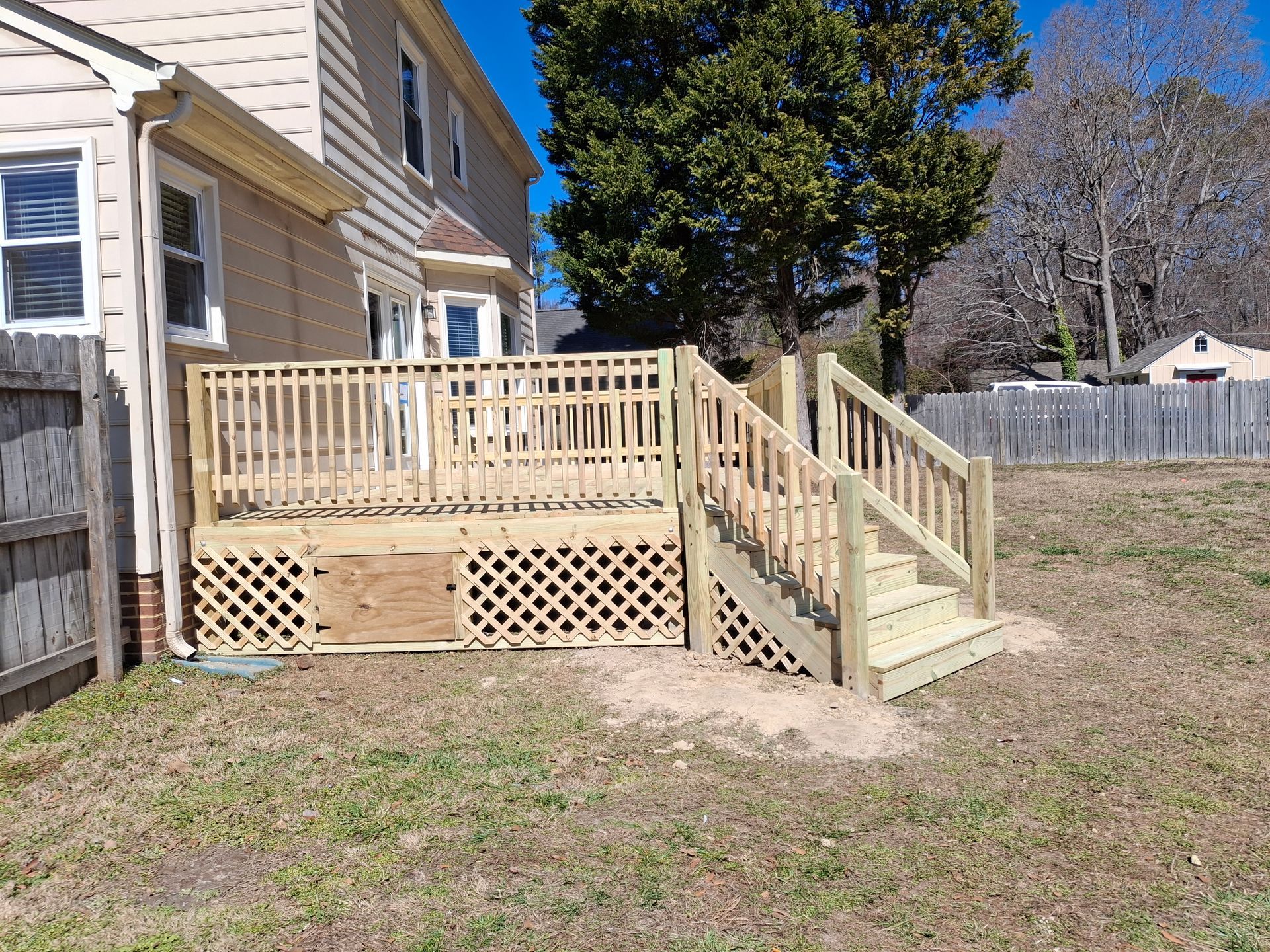 Wooden backyard deck with stairs beside a beige house and fenced yard