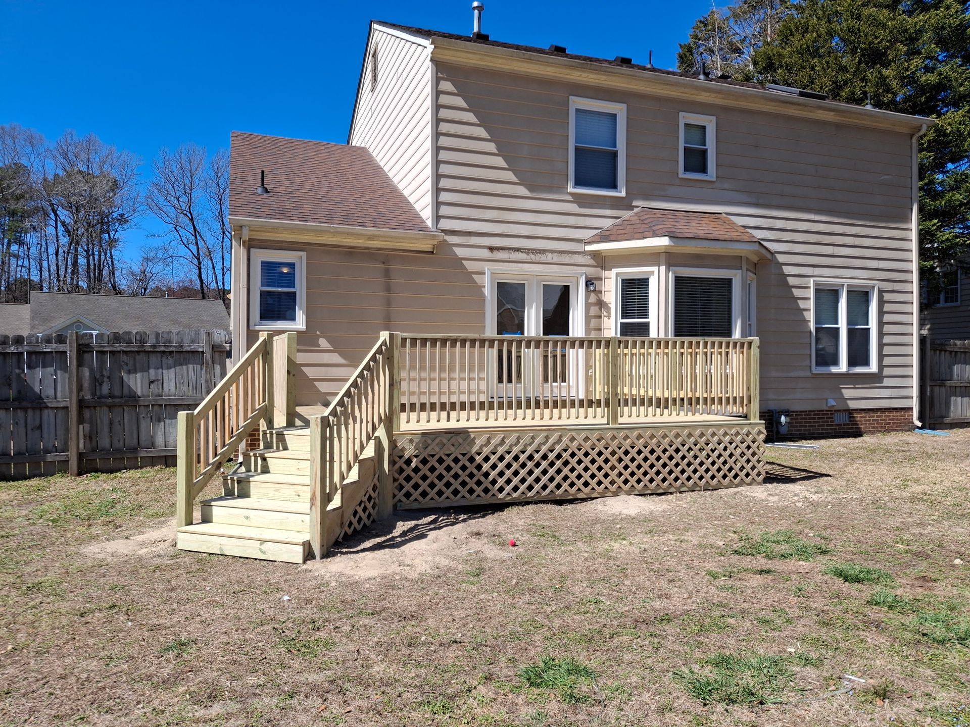 Two-story beige house with a small porch, stairs, and lattice skirting in a yard under a blue sky