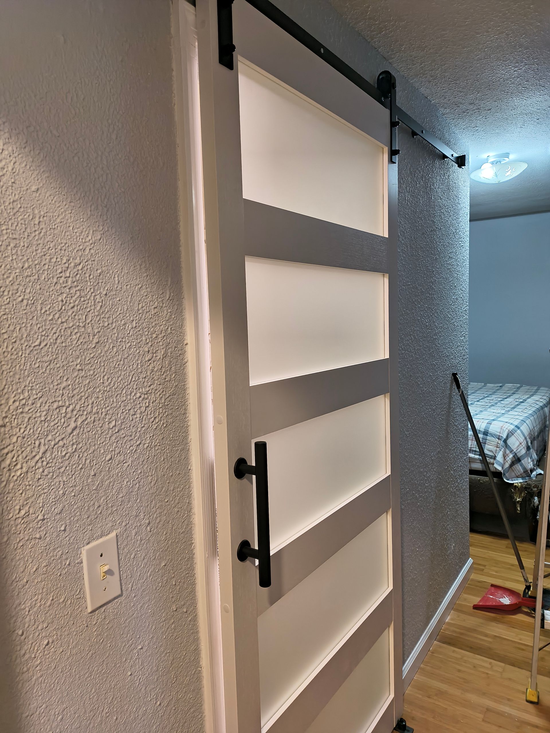 White barn-style sliding door with black handle in a home hallway, opening to a bedroom.