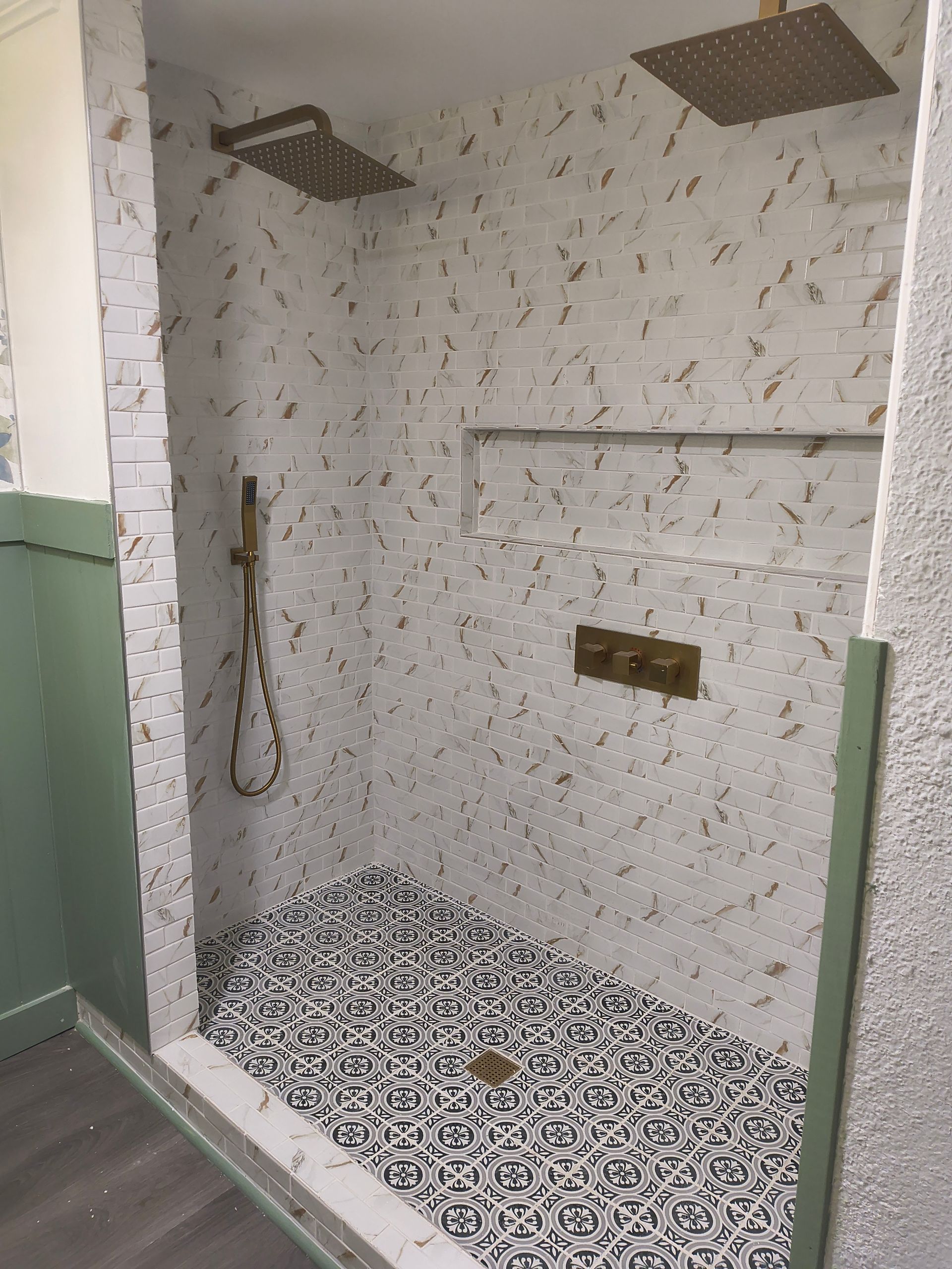 Empty tiled shower nook with two overhead showerheads and a patterned tile floor.