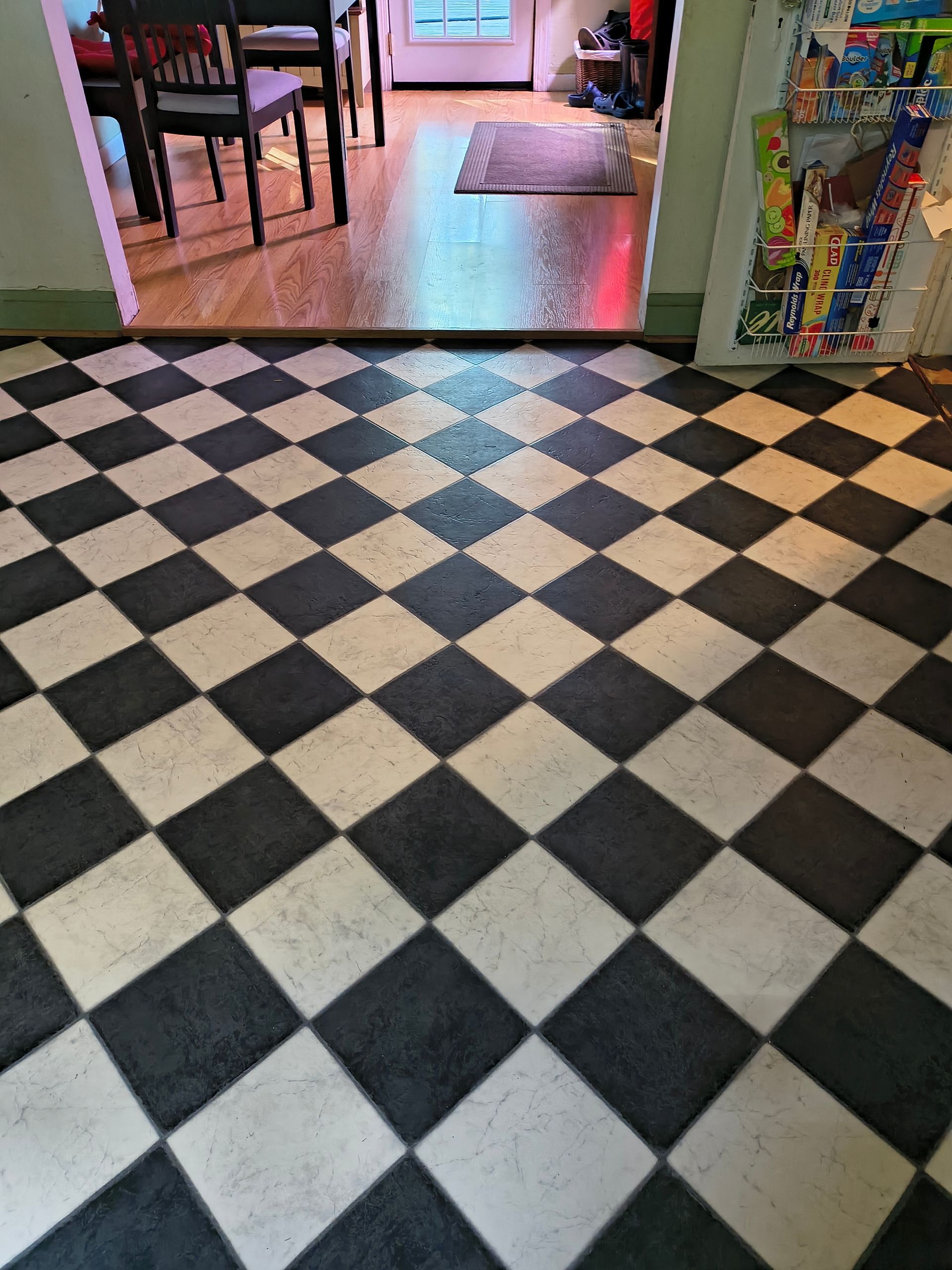 Black-and-white checkered floor leading into a dining area with chairs and a rug beyond the threshold