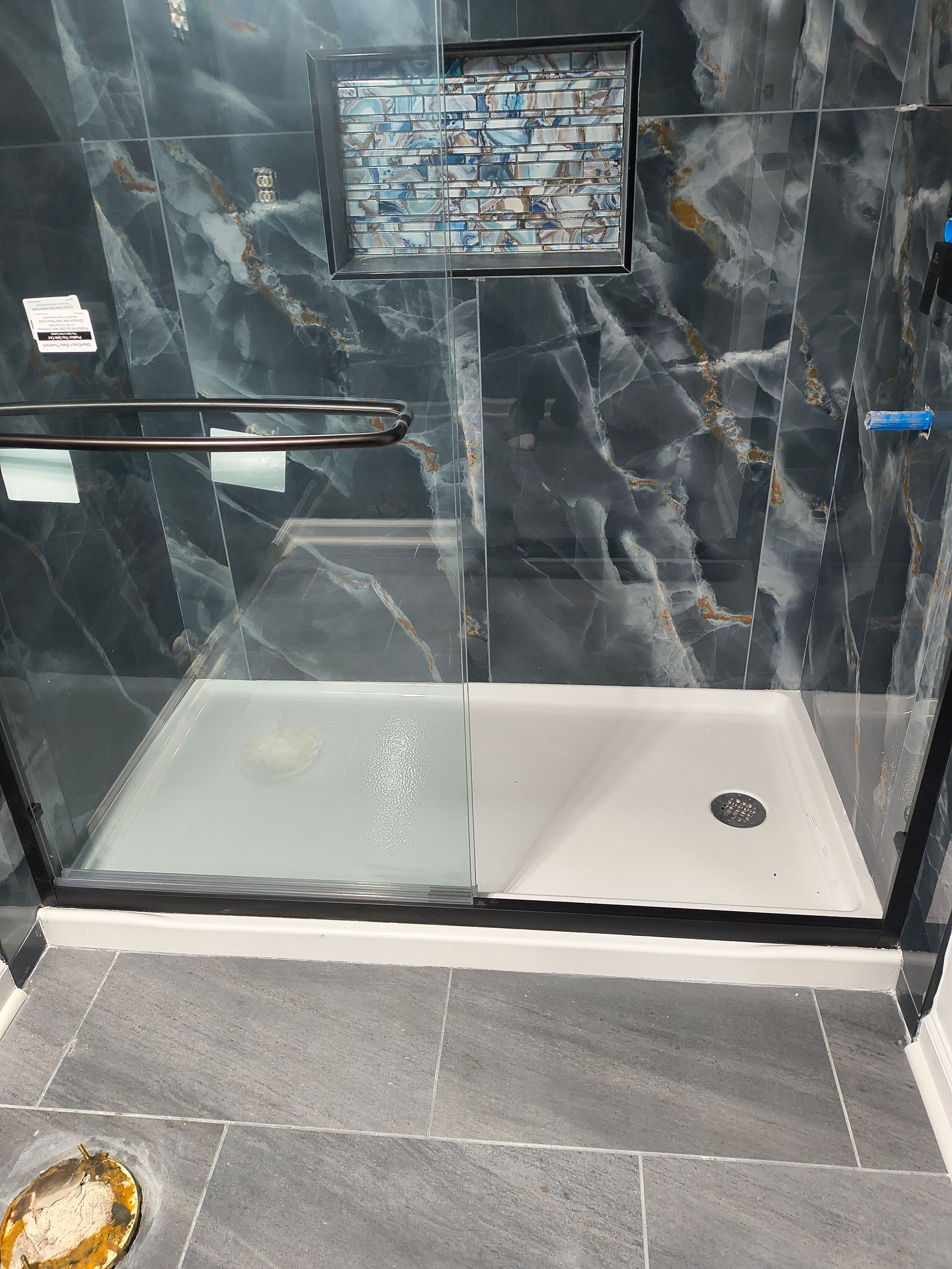 Modern black-tiled shower with glass door, white base, and wall-mounted control panel.