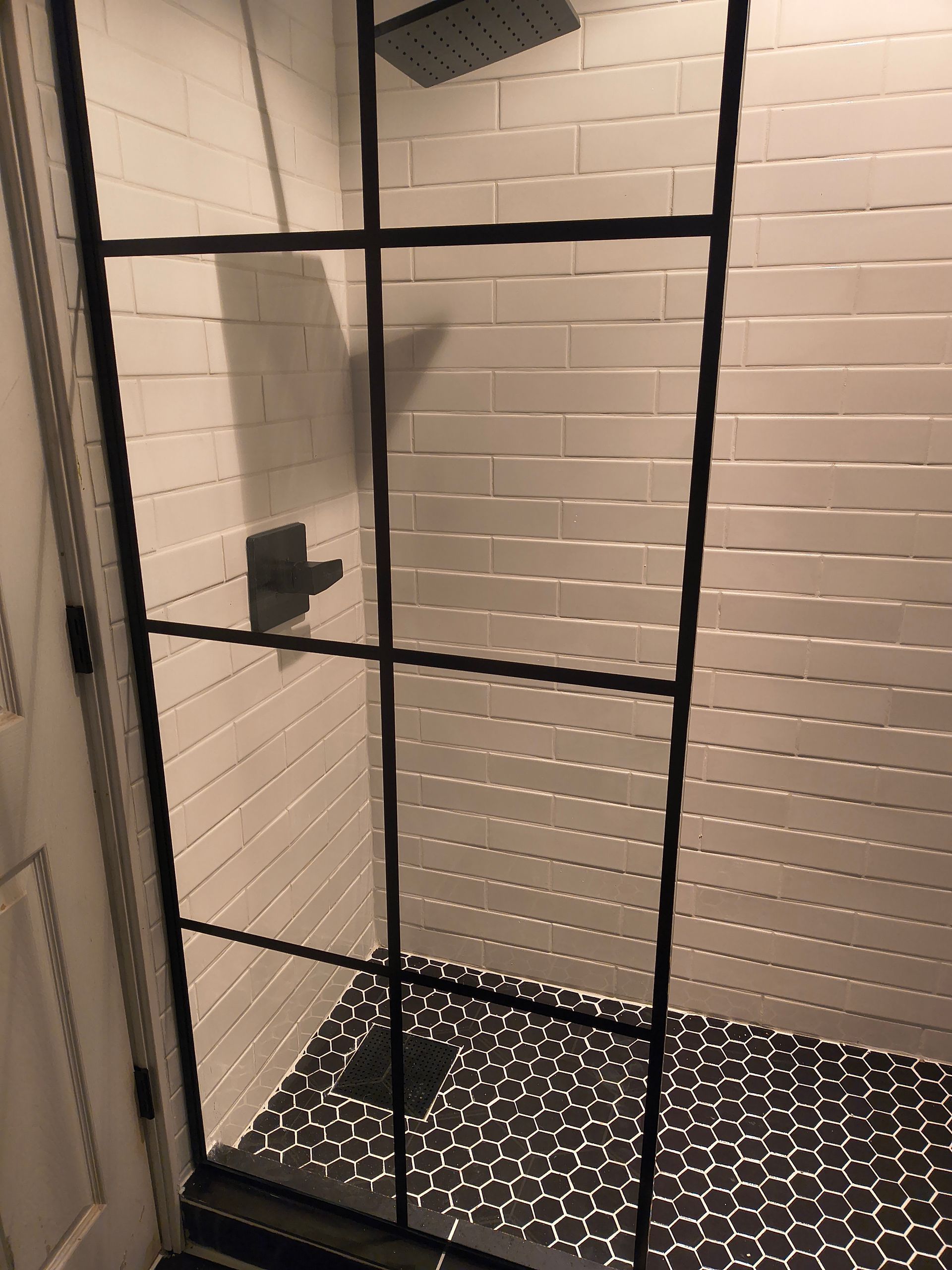 Black metal-framed shower stall with white tile walls and patterned black floor.