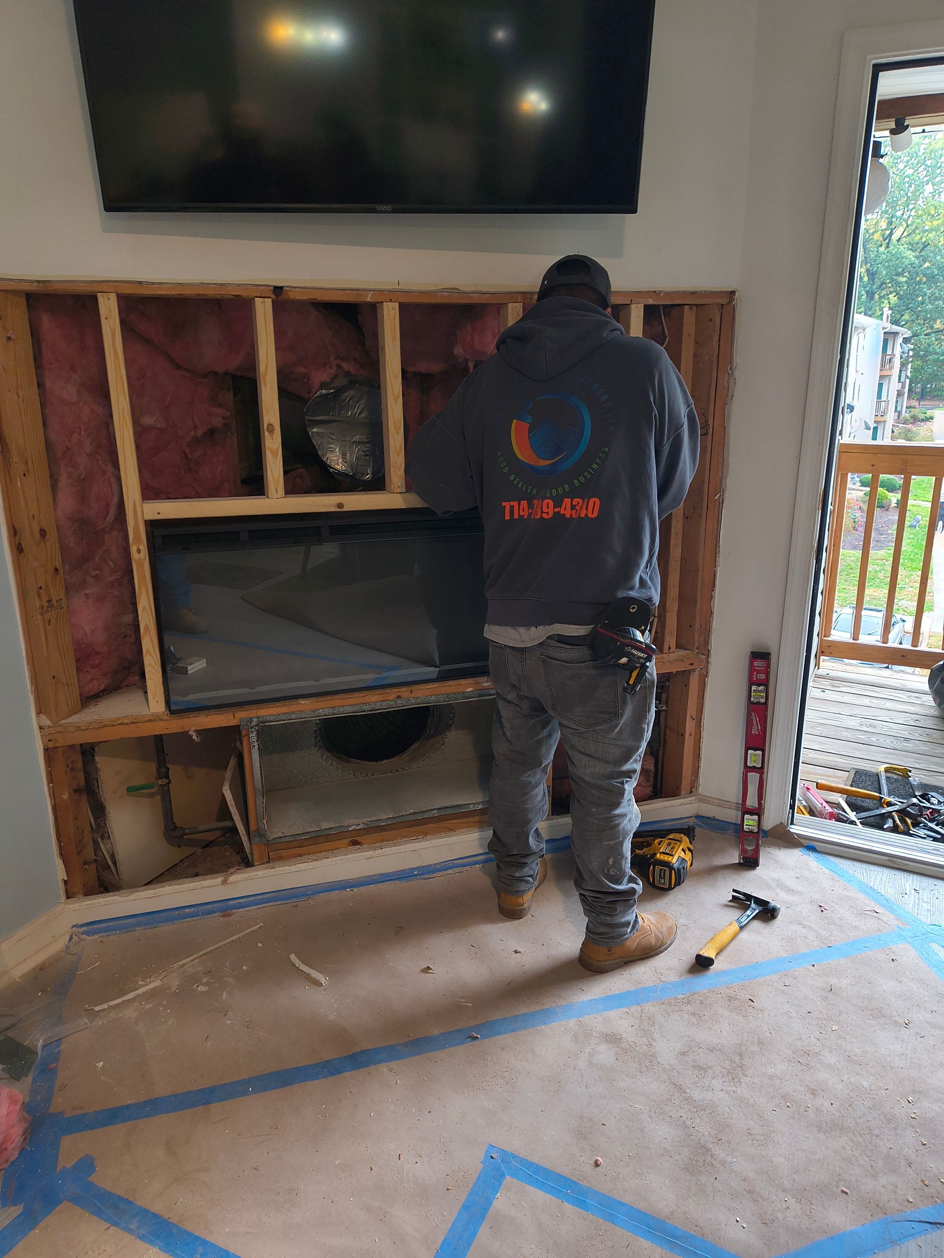 Worker installing wall-mounted TV cabinet in a room with exposed framing and tools on the floor