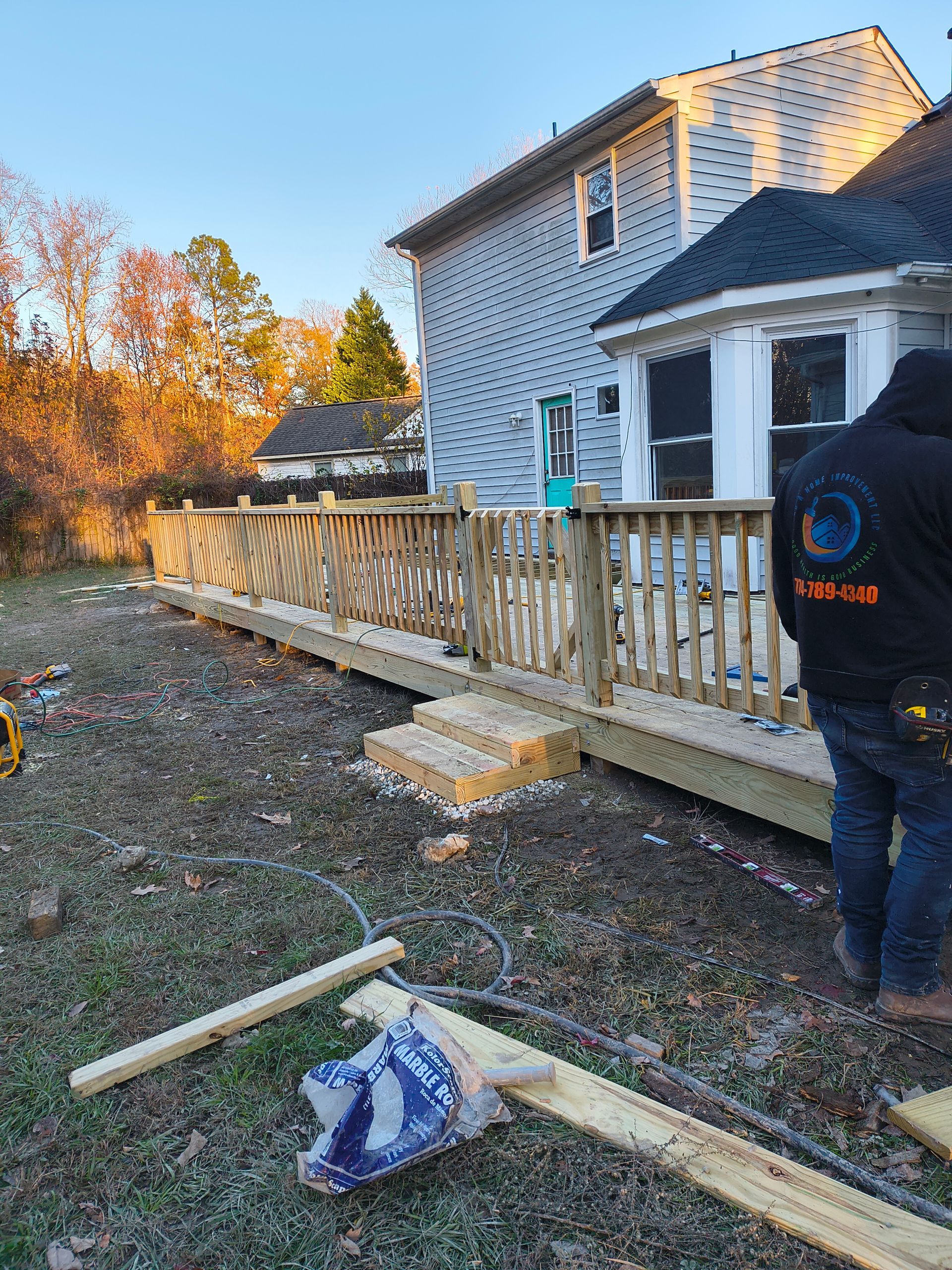 Person working on a house deck beside steps, with tools on the ground at sunset.