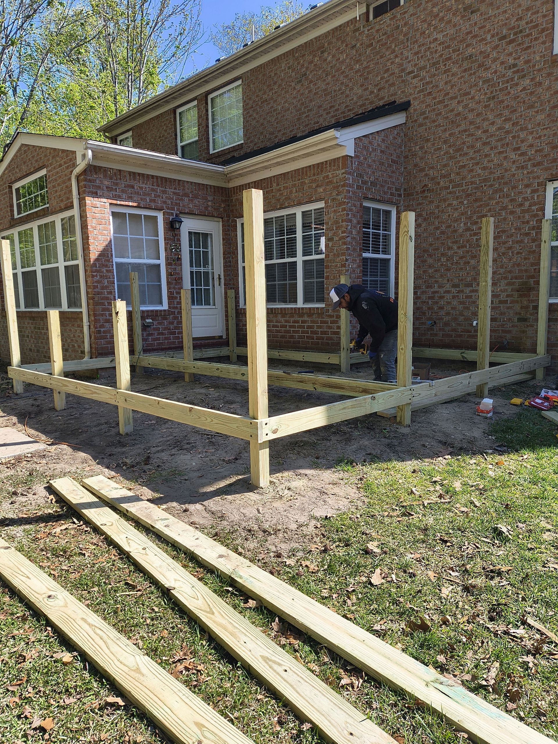 Brick house porch with new wooden ramp framing, unfinished steps, and a person standing near the door