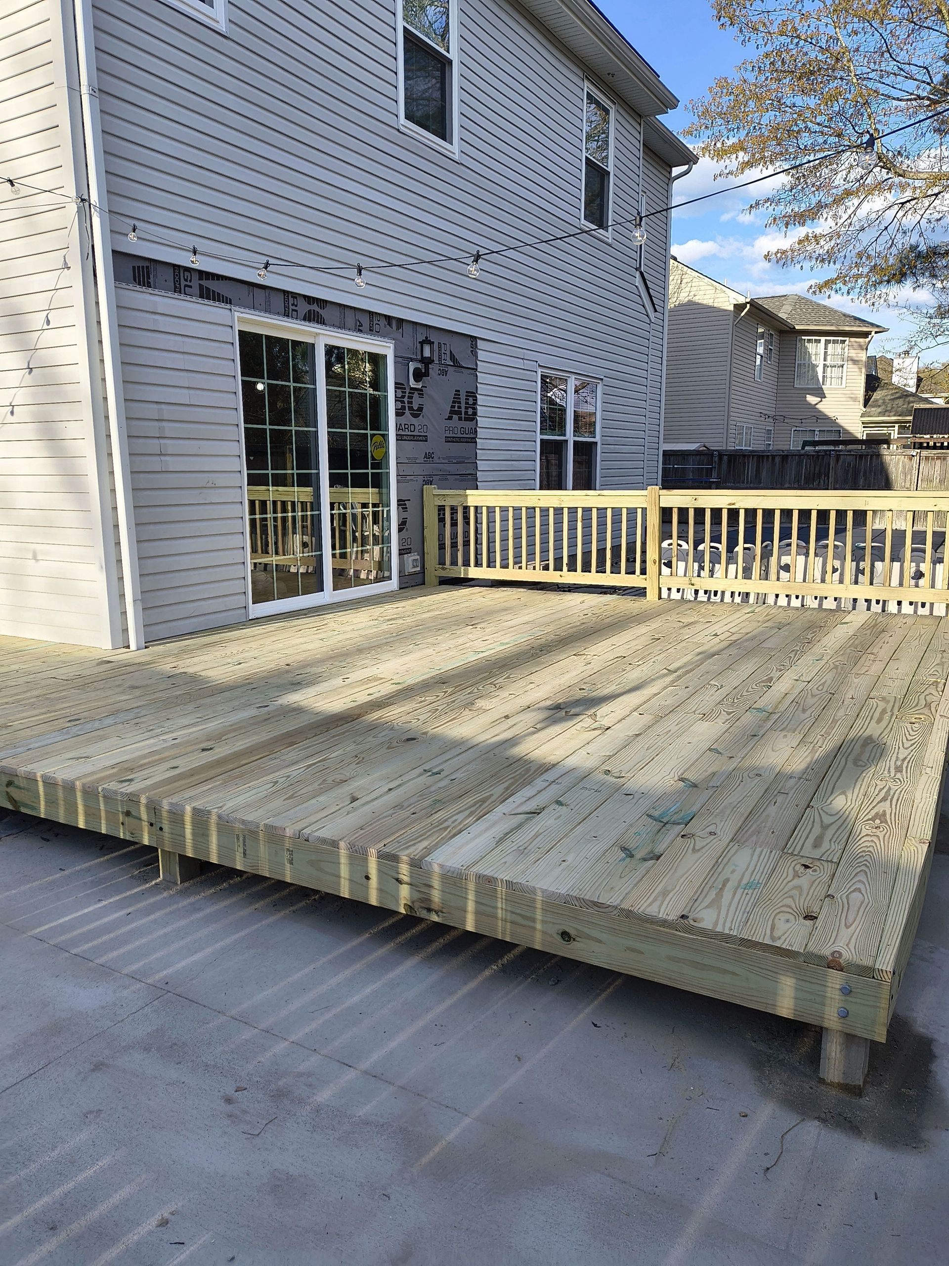 Wooden backyard deck beside a white house with sliding glass doors and railing
