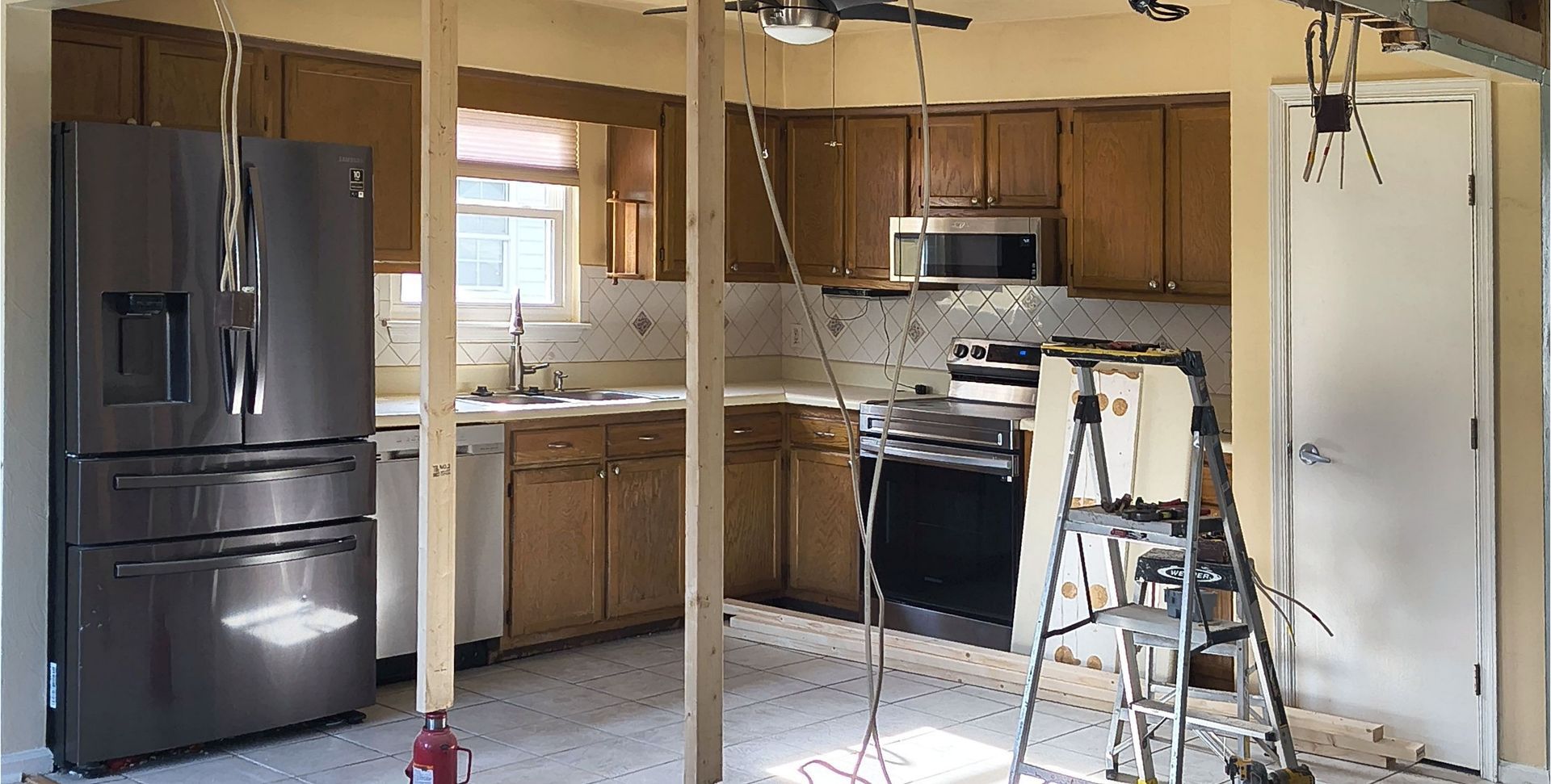 Kitchen under renovation with exposed drywall, ladder, and appliances in place