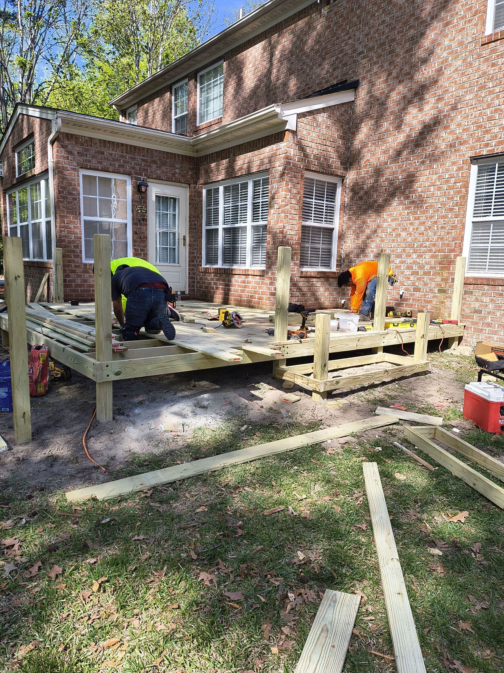 Workers building a wooden deck beside a brick house on a sunny day