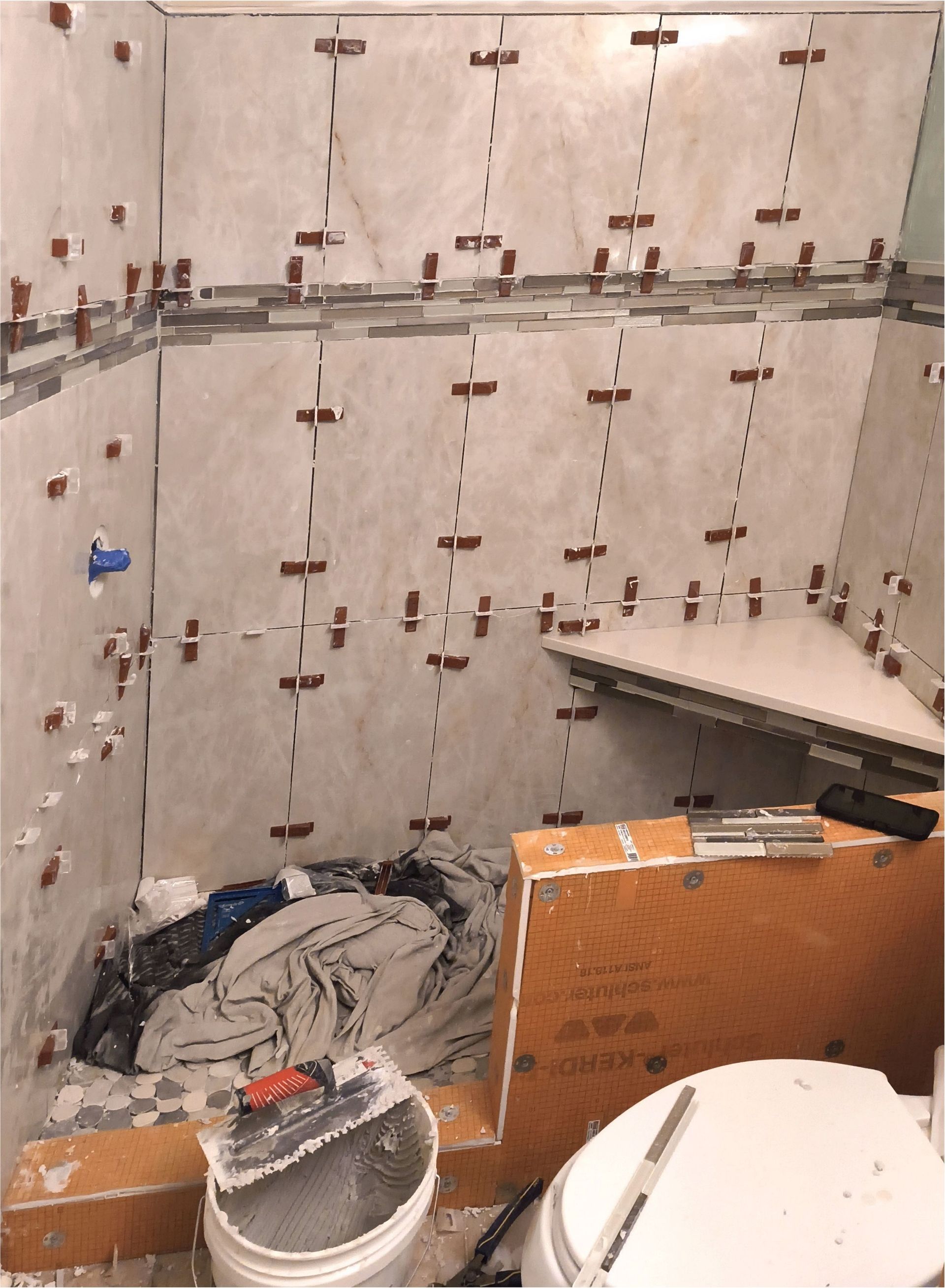 Partially tiled bathroom under construction with tools, debris, and a cardboard box on the floor