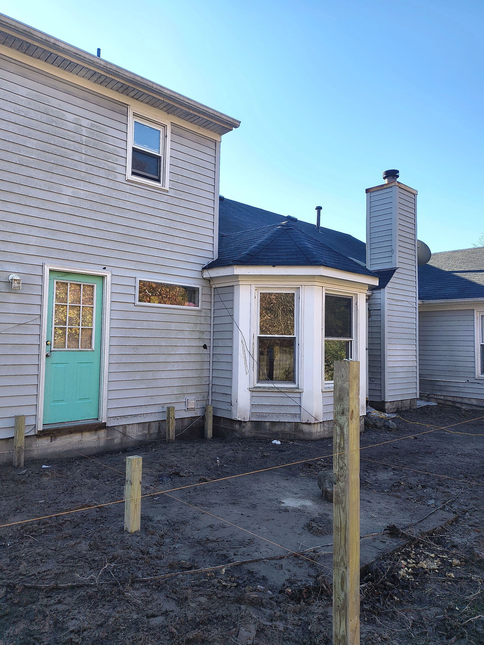 Weathered house exterior with peeling white siding, turquoise door, small windows, and a fenced gravel yard