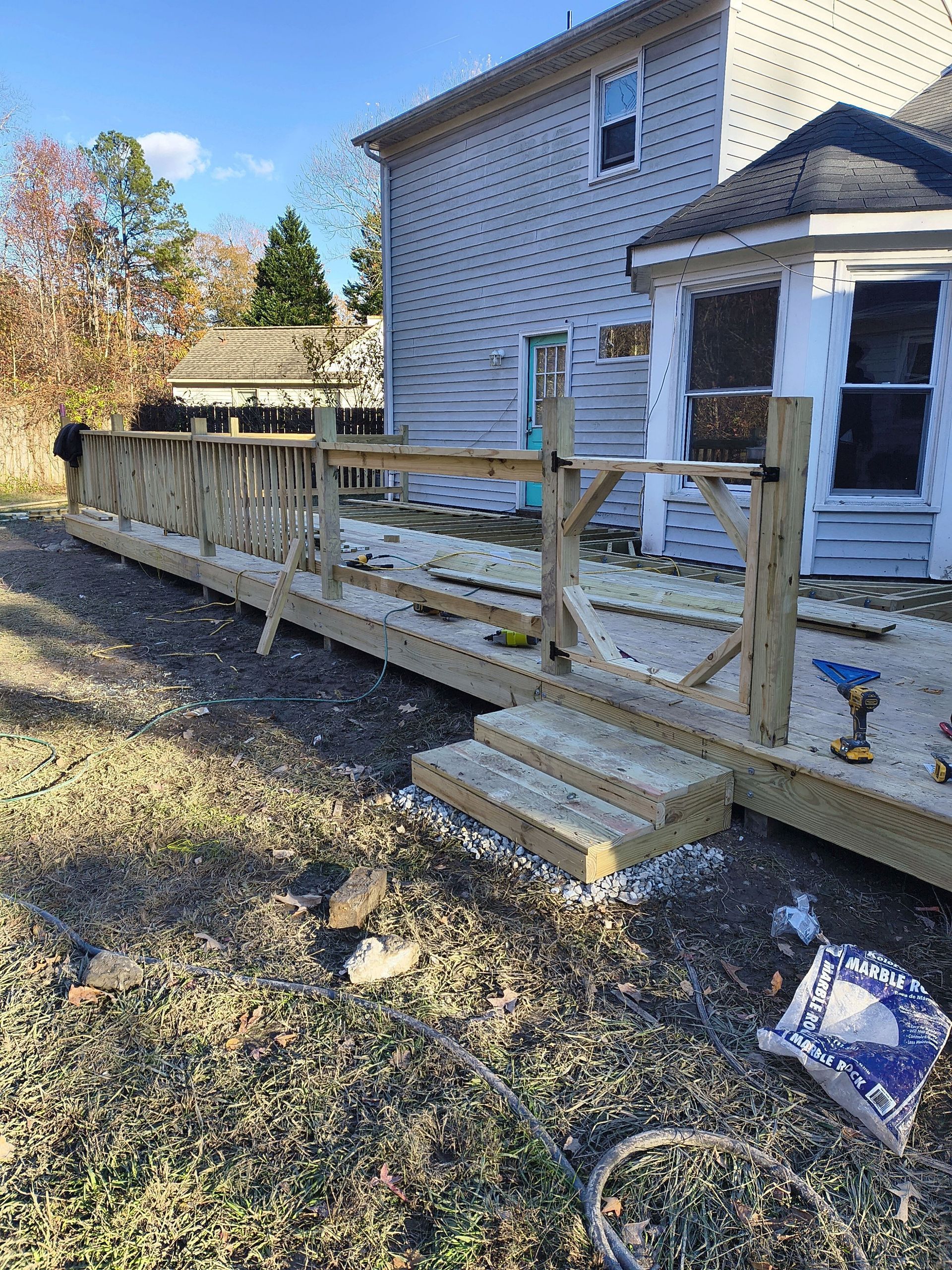 Wooden wheelchair ramp and steps beside a house with a deck and gravel yard