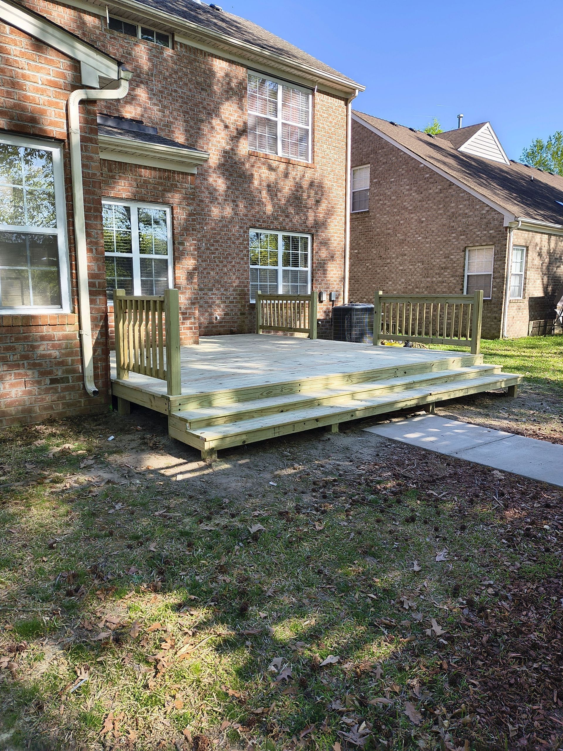 Brick house backyard with a raised wooden deck and short steps in a sunny yard