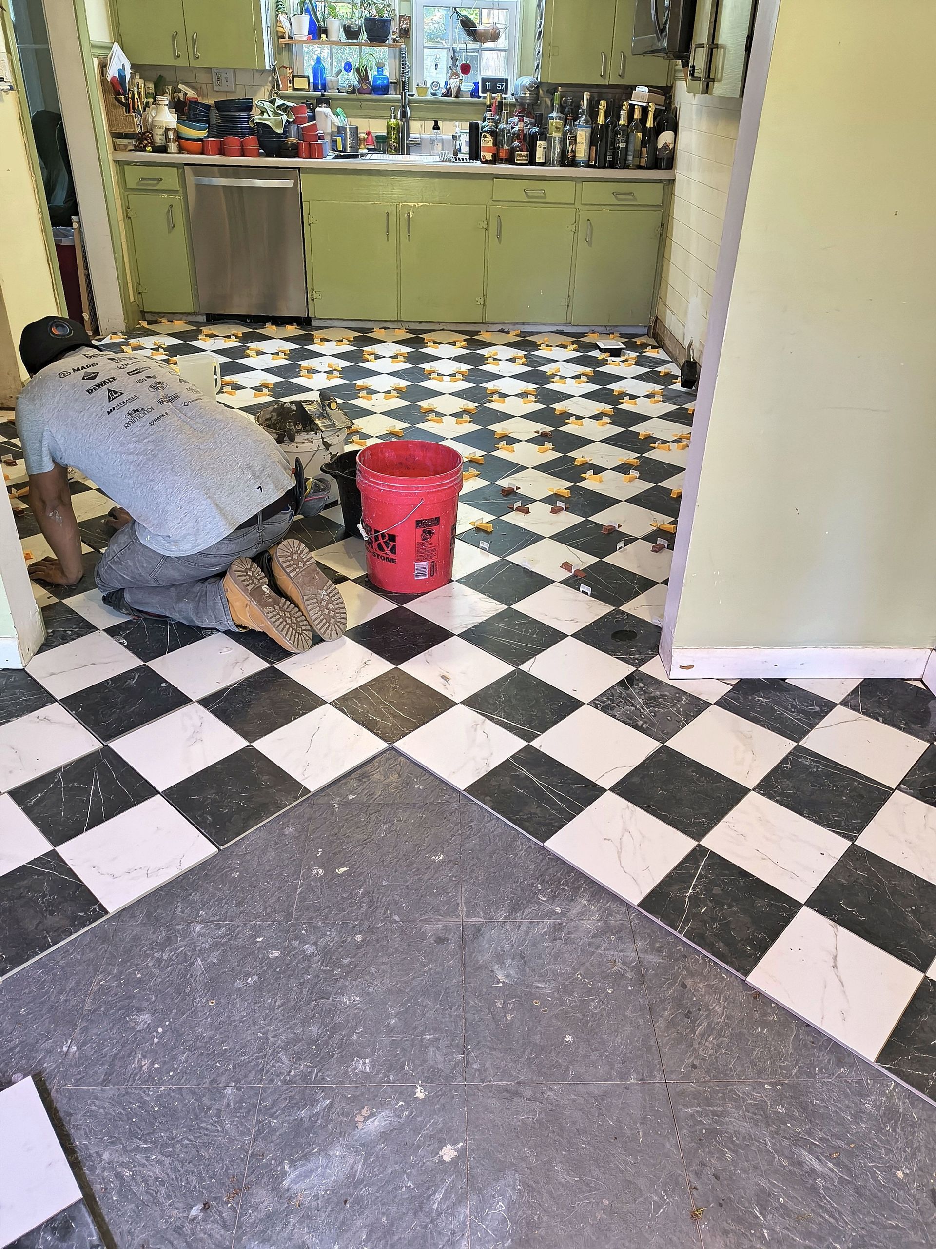 Person kneeling on a black-and-white checkered floor near a red bucket in a kitchen area